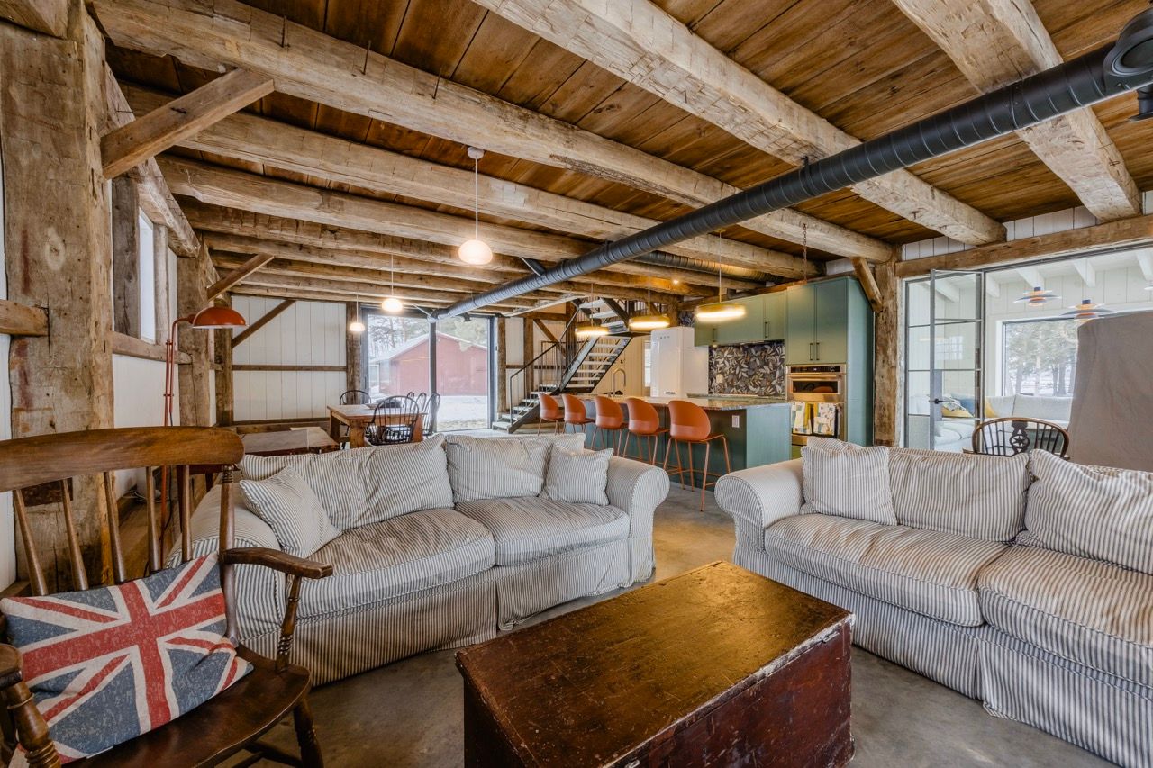 Rustic barn conversion living room with exposed beams, HVAC ductwork, and two white sofas.
