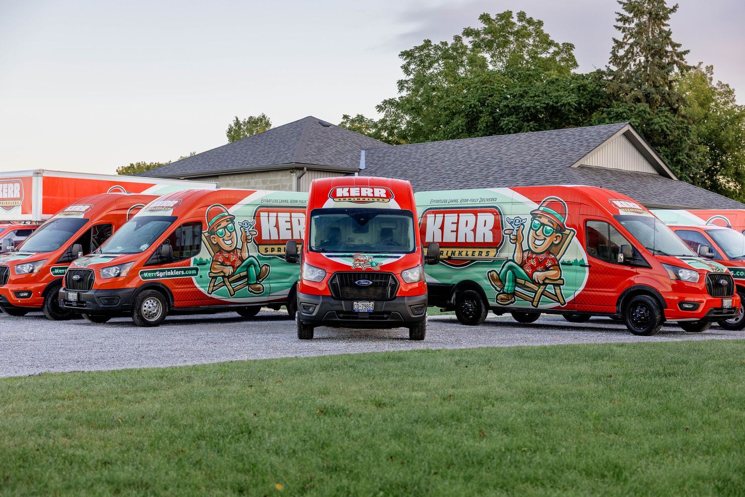 Fleet of red Kerr branded service vans parked outdoors at dusk, showcasing company branding and logo.