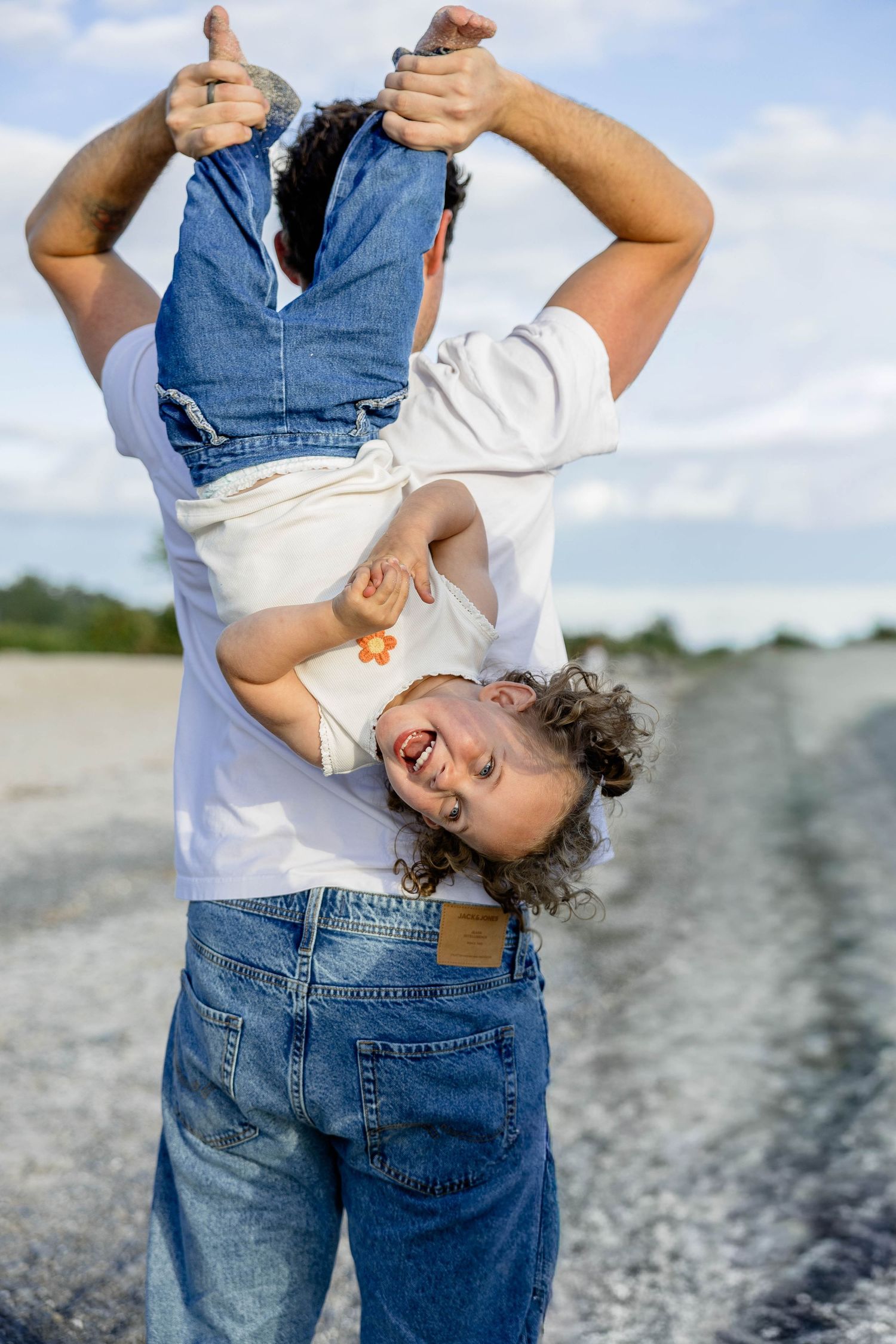 Playful father holding toddler upside down on a rocky beach, child laughing with joy.