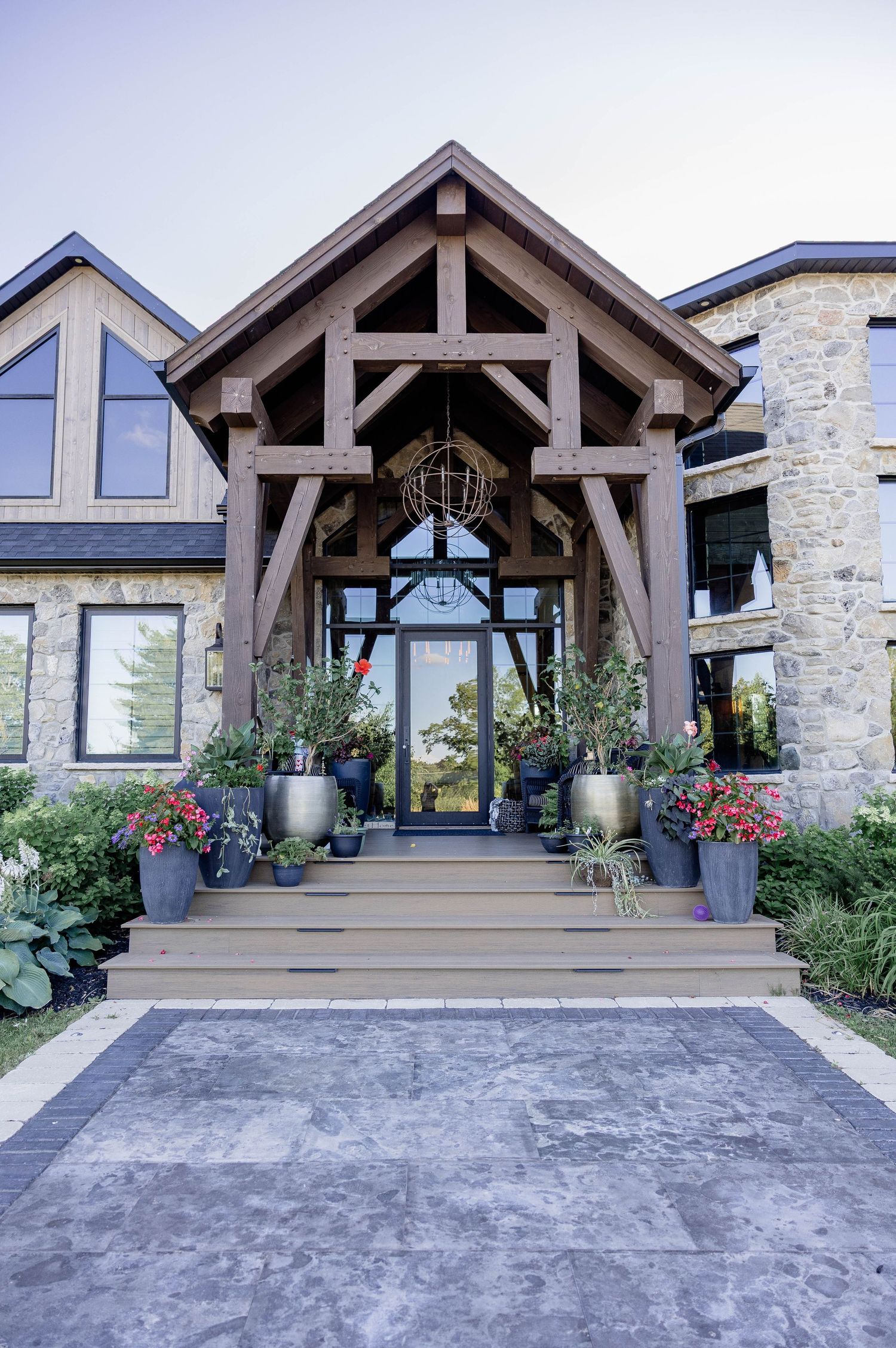 Stunning timber frame home entrance with stone exterior, potted plants, and decorative globe chandelier.
