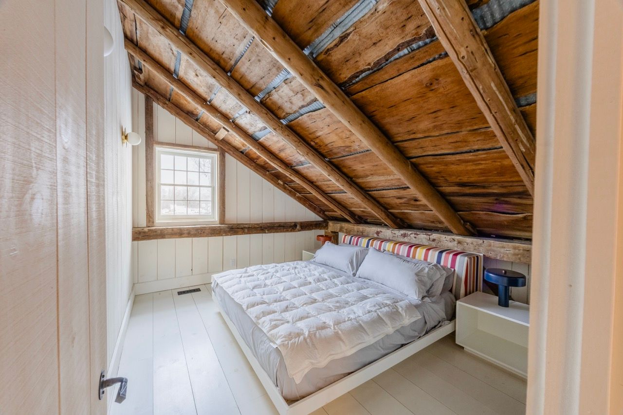 Cozy attic bedroom with exposed wood beam ceiling, white floors, and a double bed.