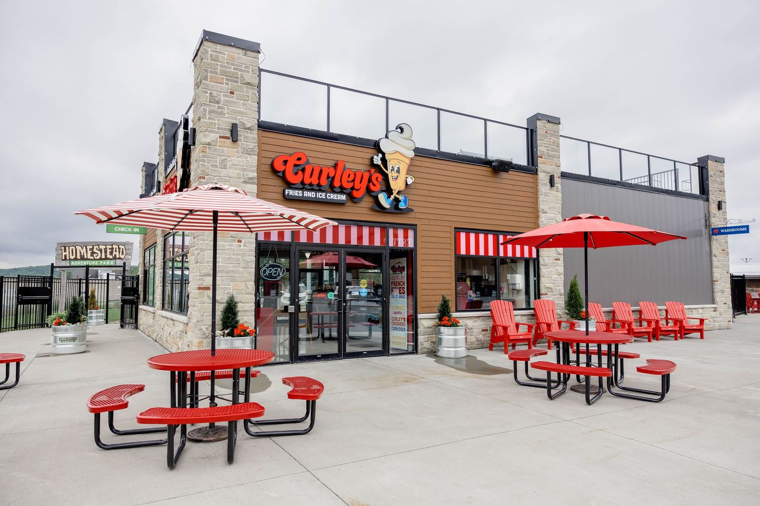 Exterior of Curley's fast food restaurant with red outdoor picnic tables and striped umbrellas on patio.