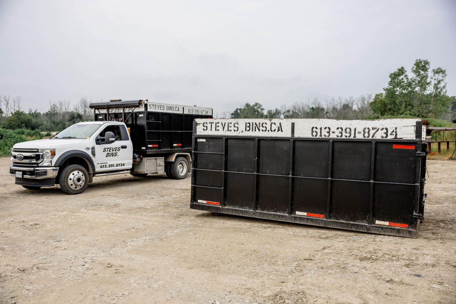 Steve's Bins truck and large black roll-off dumpster rental container in a gravel lot, phone 613-391-8234.
