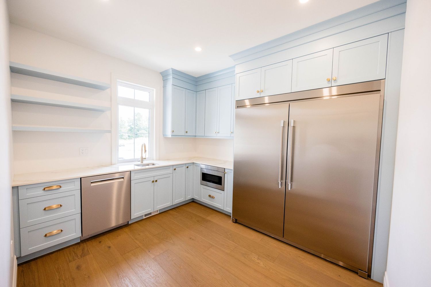 Modern kitchen with light blue cabinets, stainless steel appliances, gold hardware, and hardwood floors.