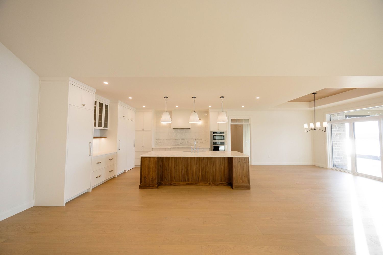 Modern open kitchen with walnut island, white cabinetry, pendant lights, and light hardwood floors.