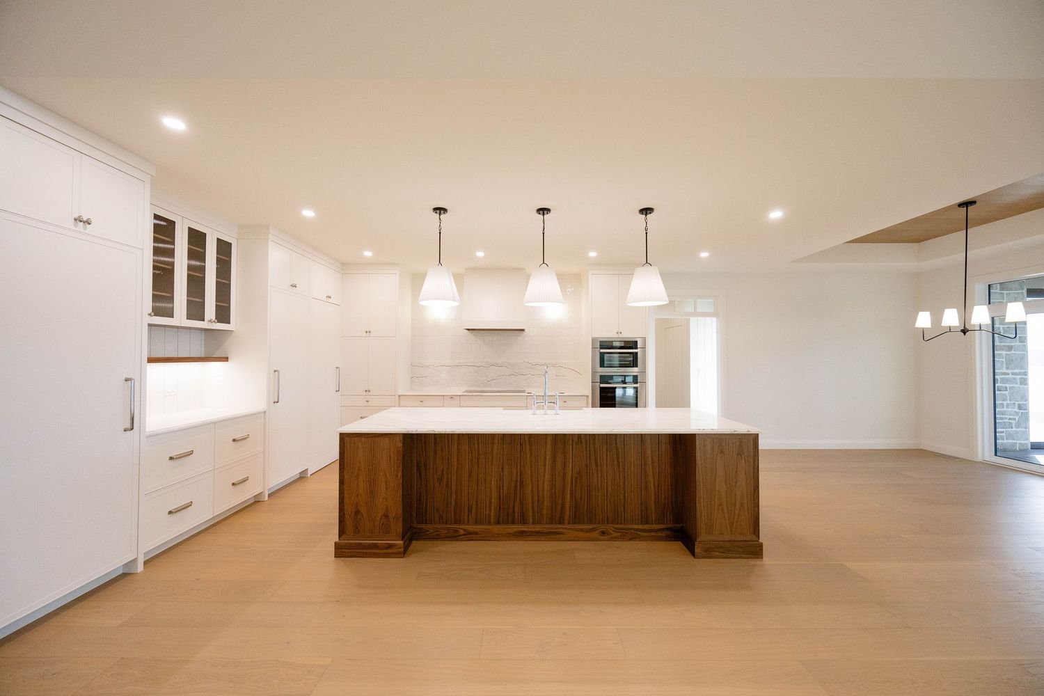 Modern open-plan kitchen with white cabinetry, walnut island, pendant lights, and light hardwood floors.