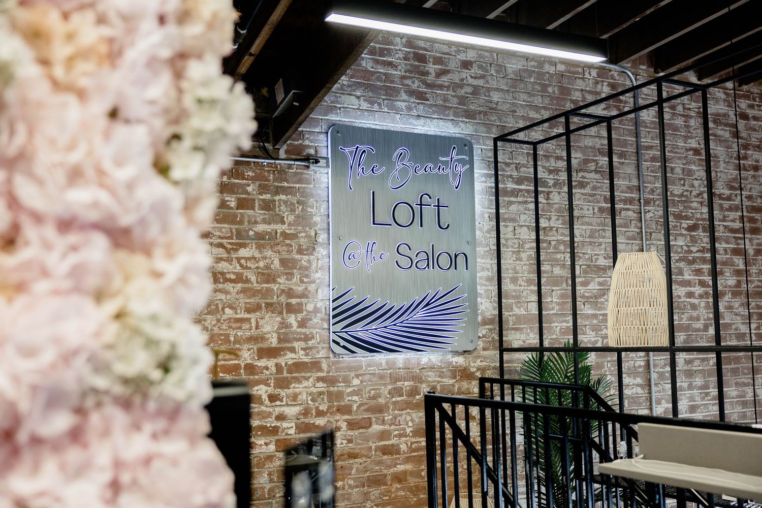 Elegant Beauty Loft Salon sign on exposed brick wall with floral decor and industrial black railing.