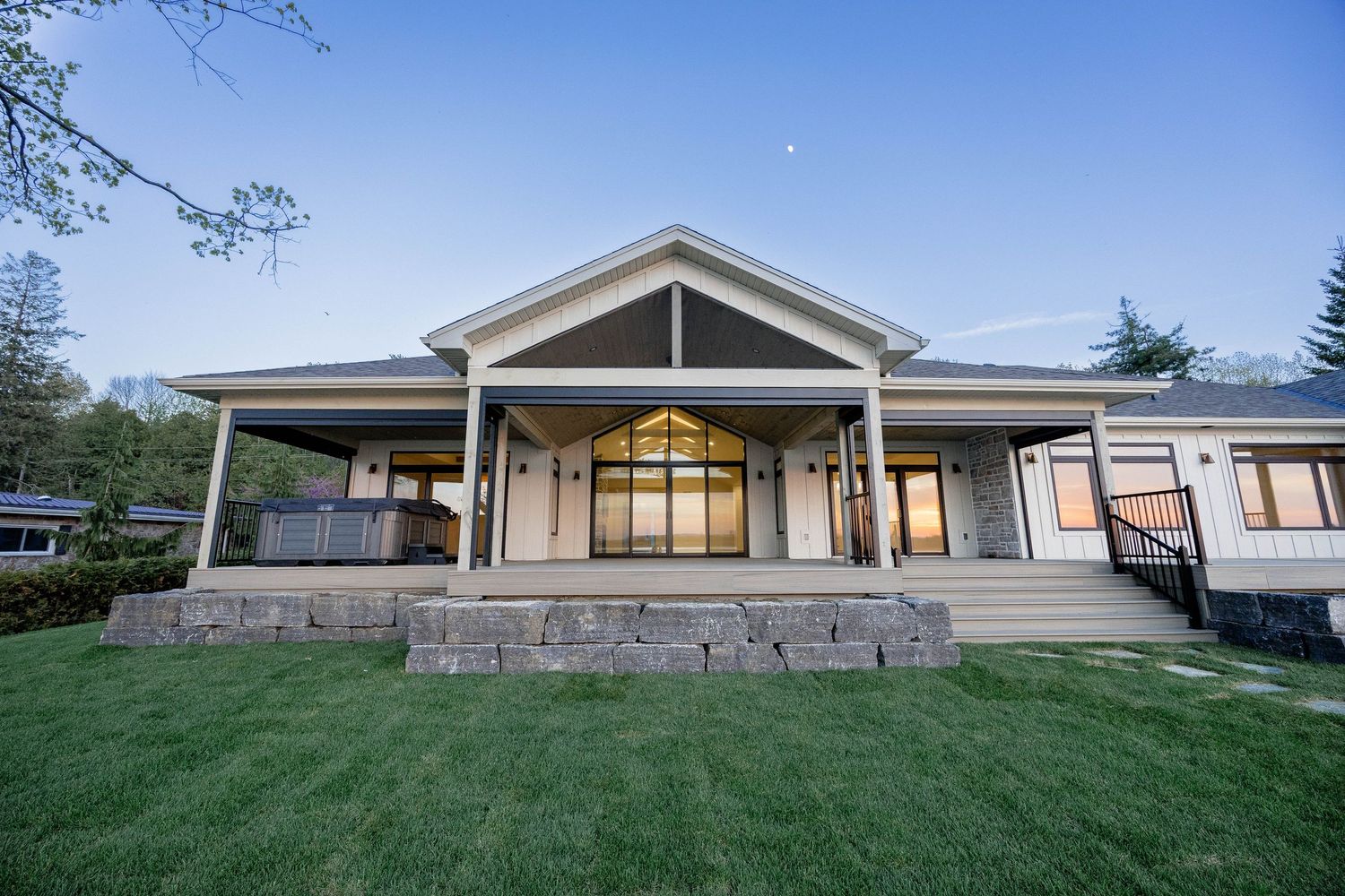 Charming ranch-style home with covered porch, stone steps, and lush green lawn at dusk.