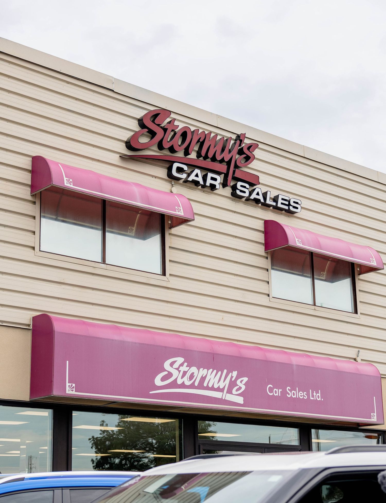 Exterior of Stormy's Car Sales Ltd. building featuring pink awnings and bold signage.