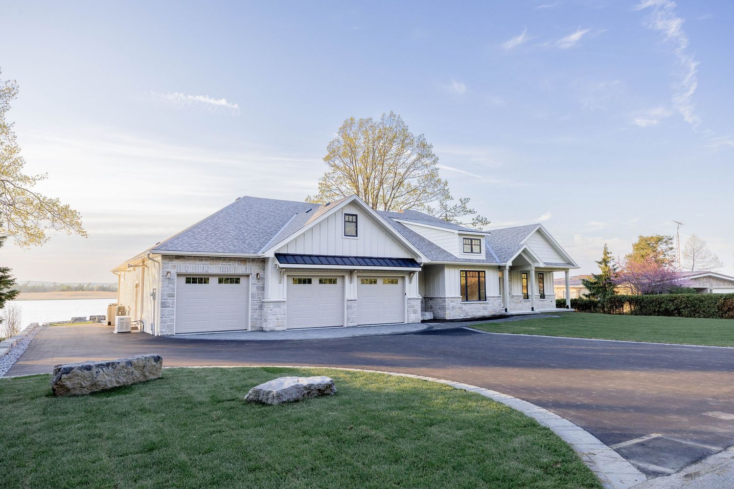 White luxury home with three-car garage beside a serene waterfront at golden hour.