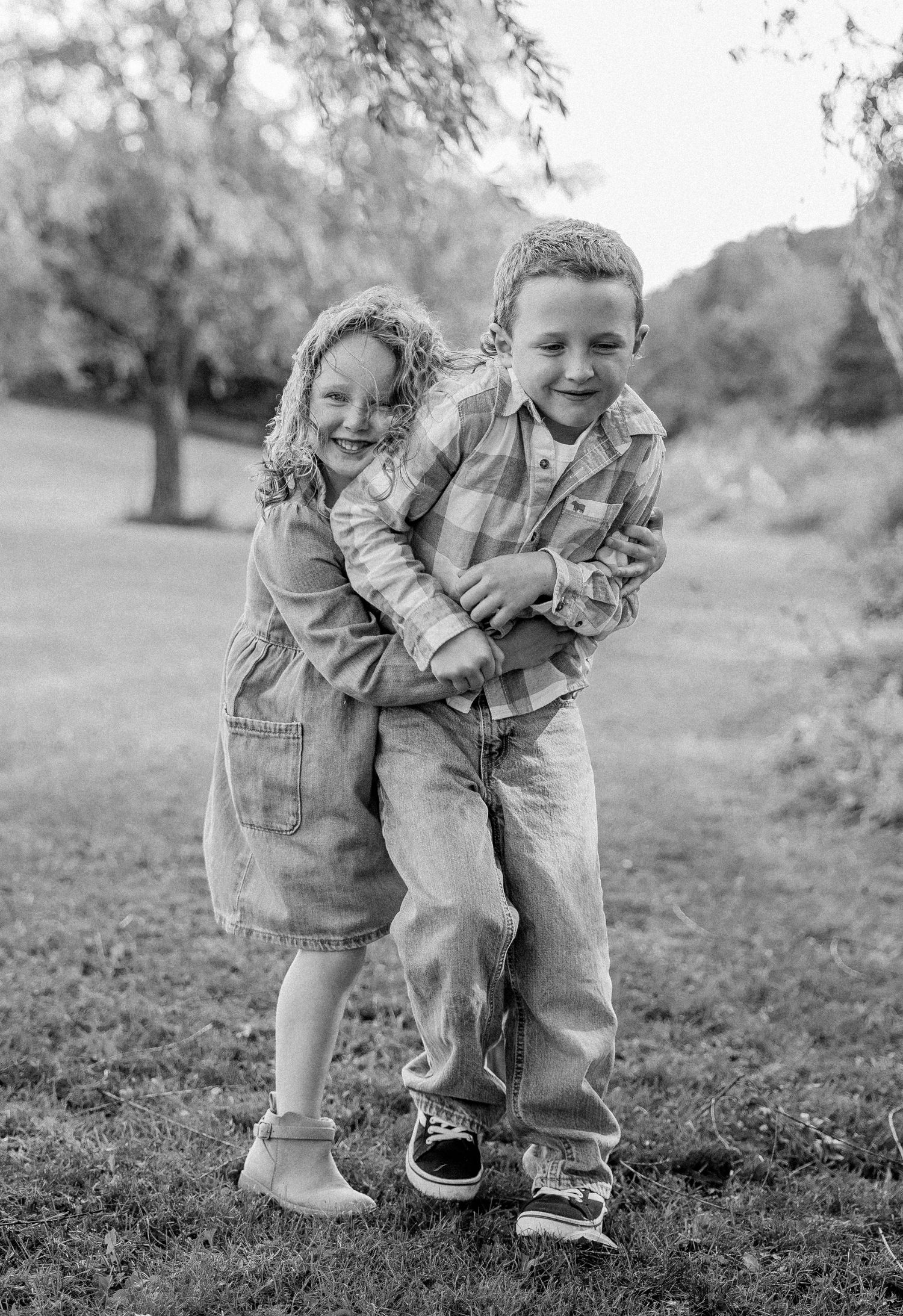 Two happy children hugging and laughing outdoors in a park, black and white photo.