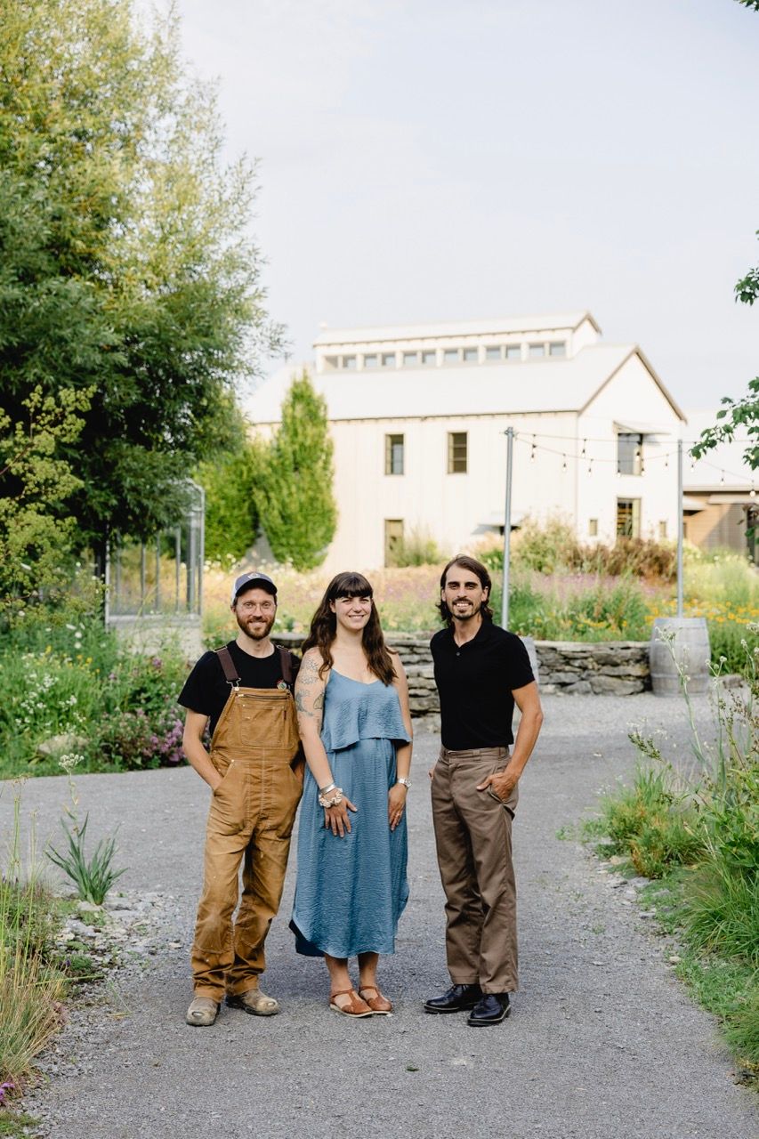 Three people posing together on garden path with white building in background.