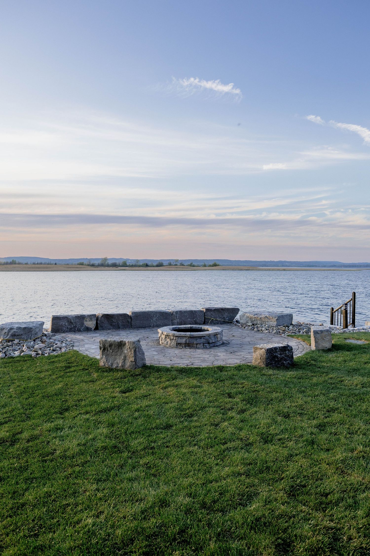 Serene waterfront fire pit area with stone seating and panoramic lake views at sunset.