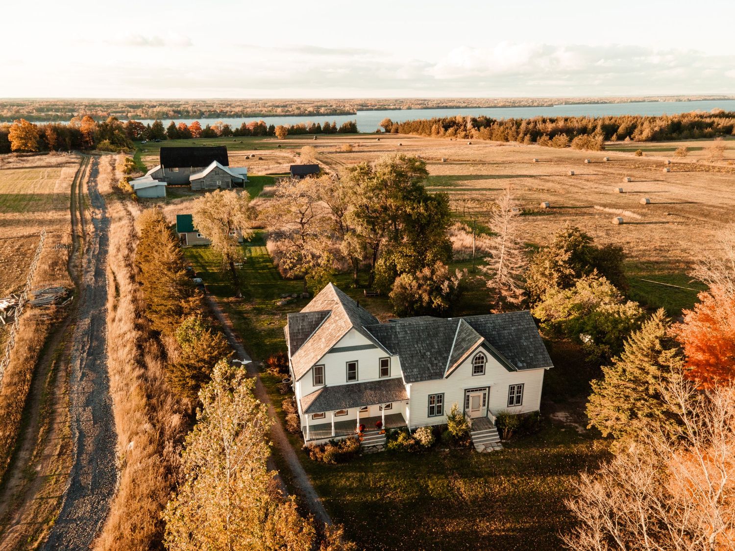 Aerial autumn view of a white farmhouse surrounded by colorful trees and open agricultural fields.