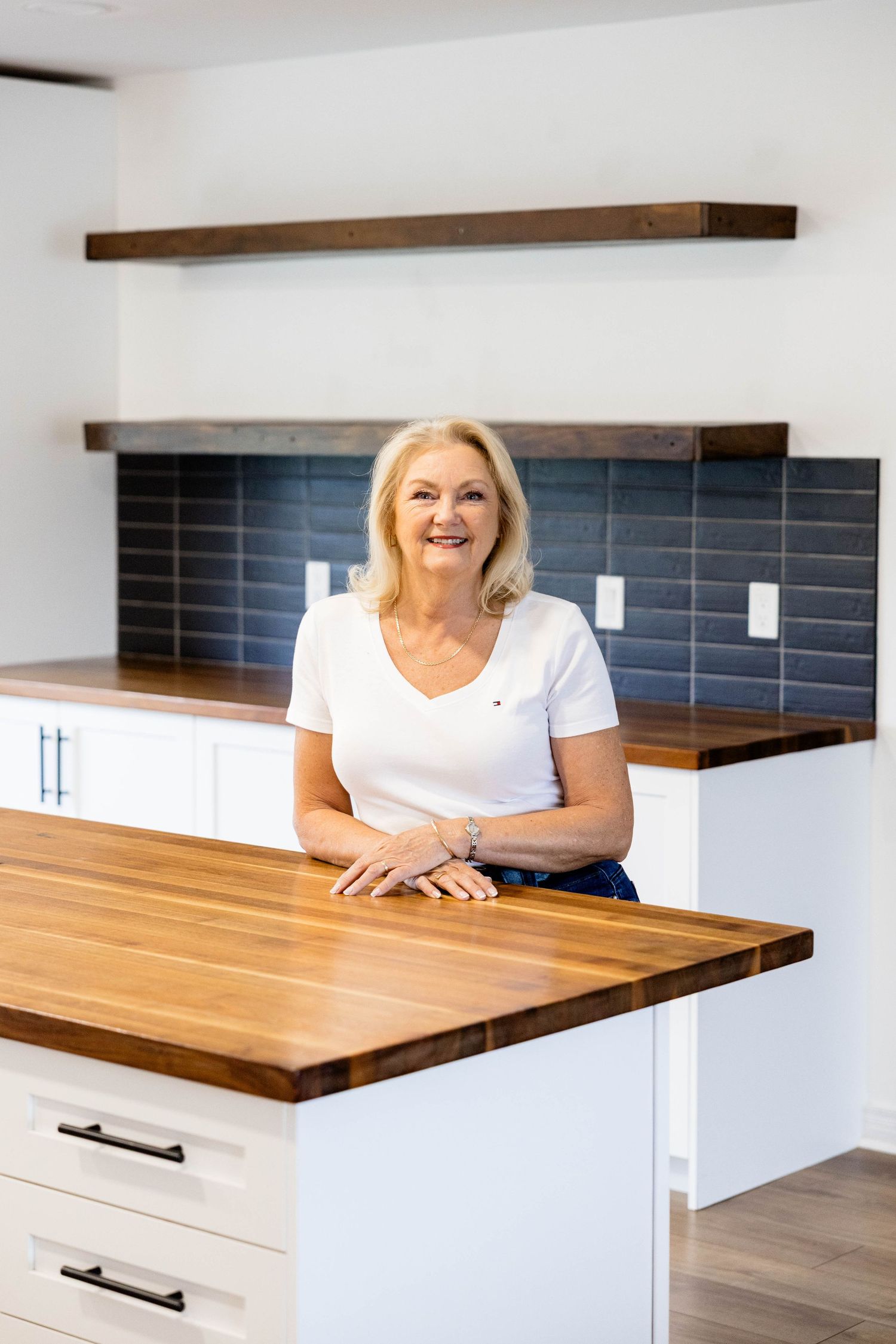 Blonde woman leaning on kitchen island with butcher block countertop and blue tile backsplash.