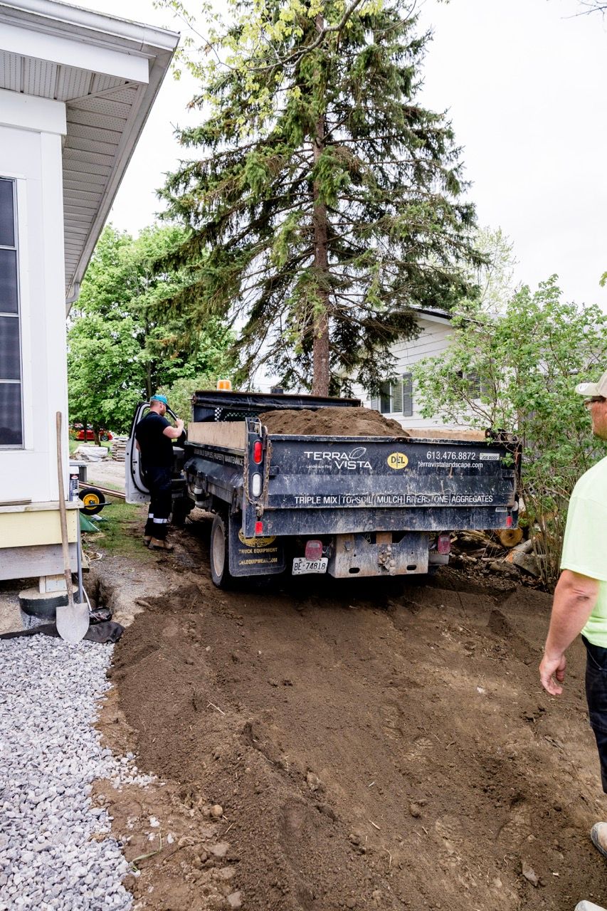 Workers unloading dirt from Terra Vista dump truck beside white house and gravel driveway.