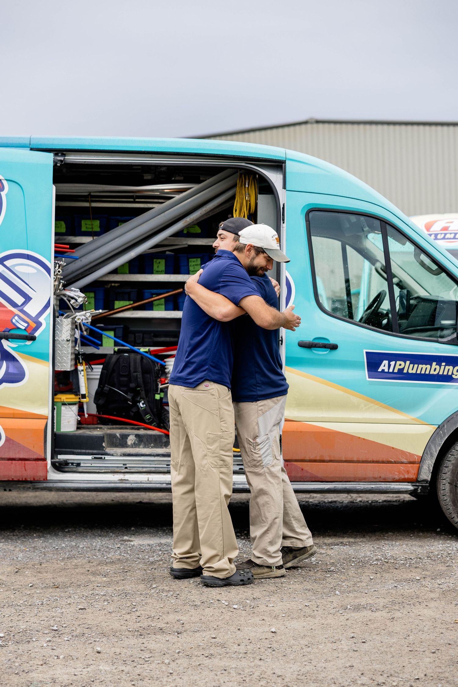 Two A1 Plumbing technicians hugging beside a branded service van with open doors.