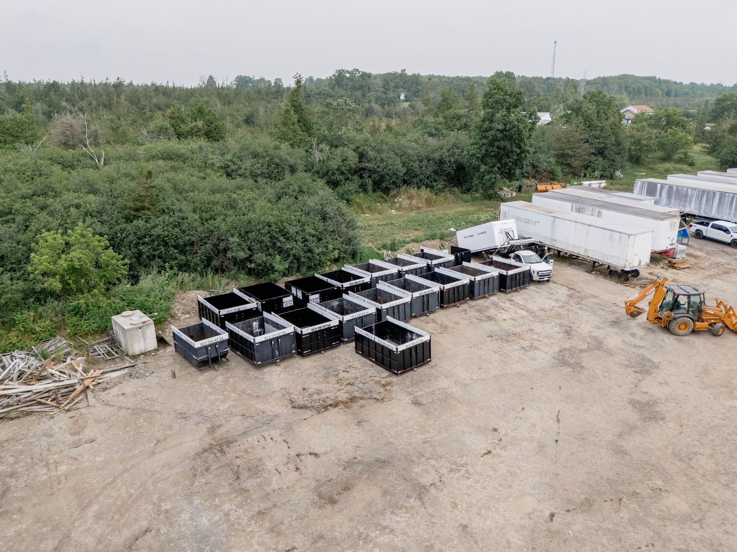 Aerial view of black modular concrete forms arranged in rows on a gravel lot with trees and construction equipment in background.
