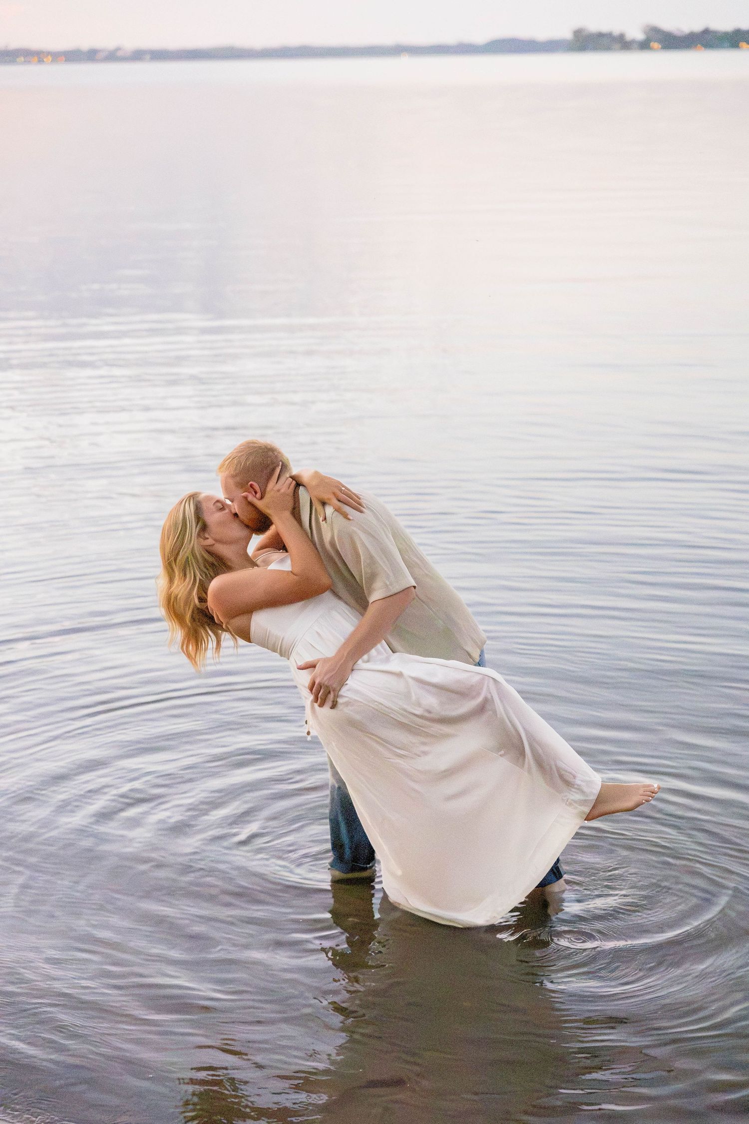 Romantic couple kissing while standing in calm lake water at sunset.
