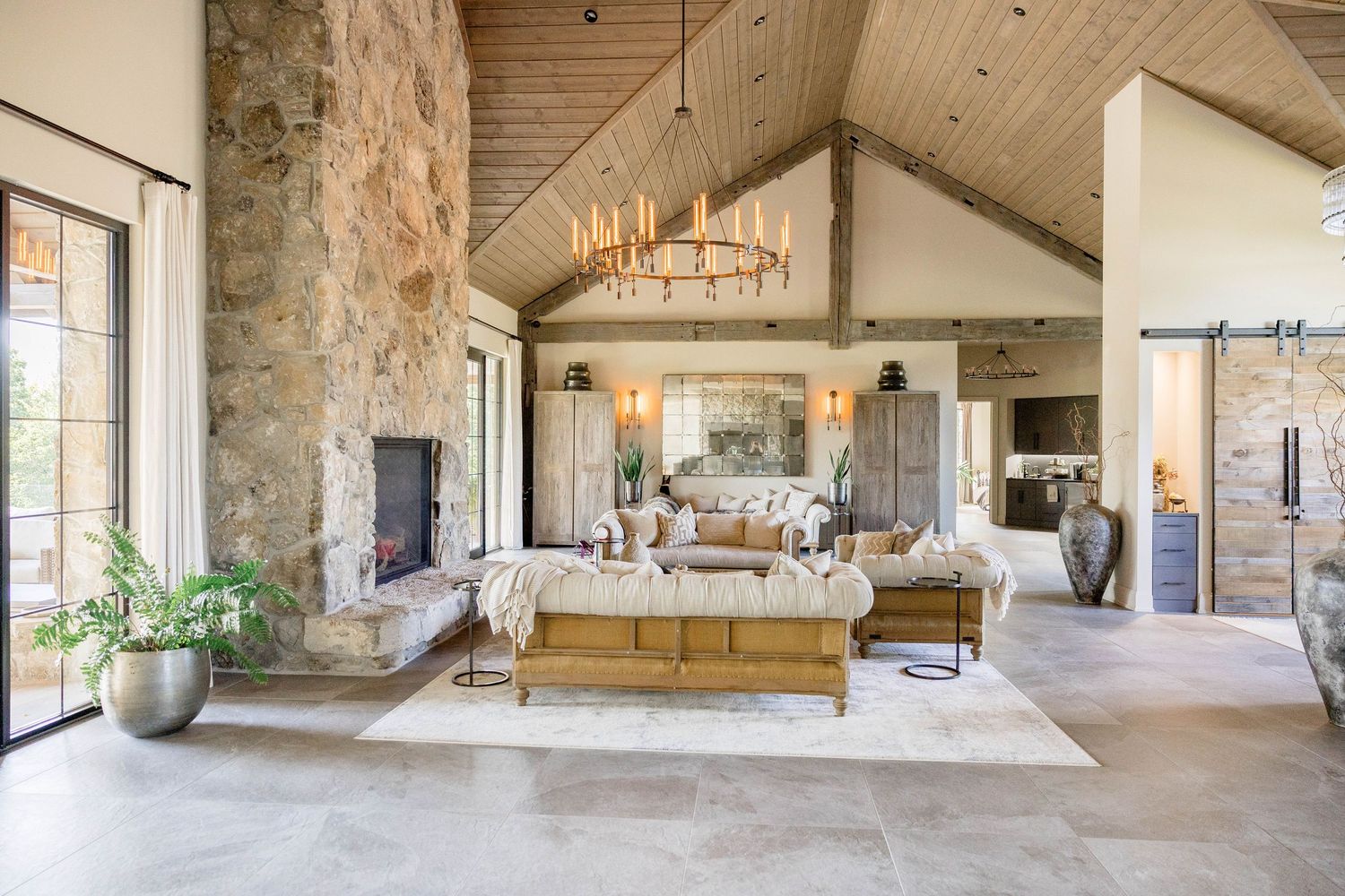 Rustic luxury living room with vaulted wood ceiling, stone fireplace, chandelier, and neutral furnishings.