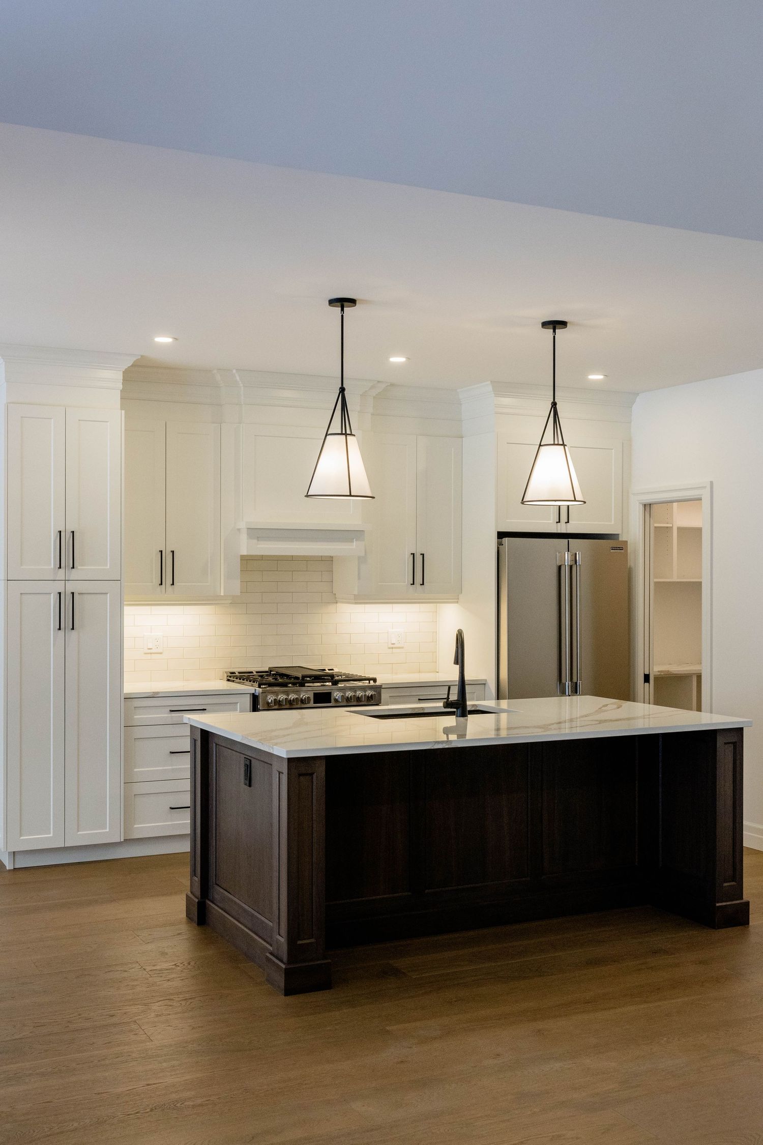 Elegant white kitchen with dark wood island, geometric pendant lights, and stainless steel refrigerator.