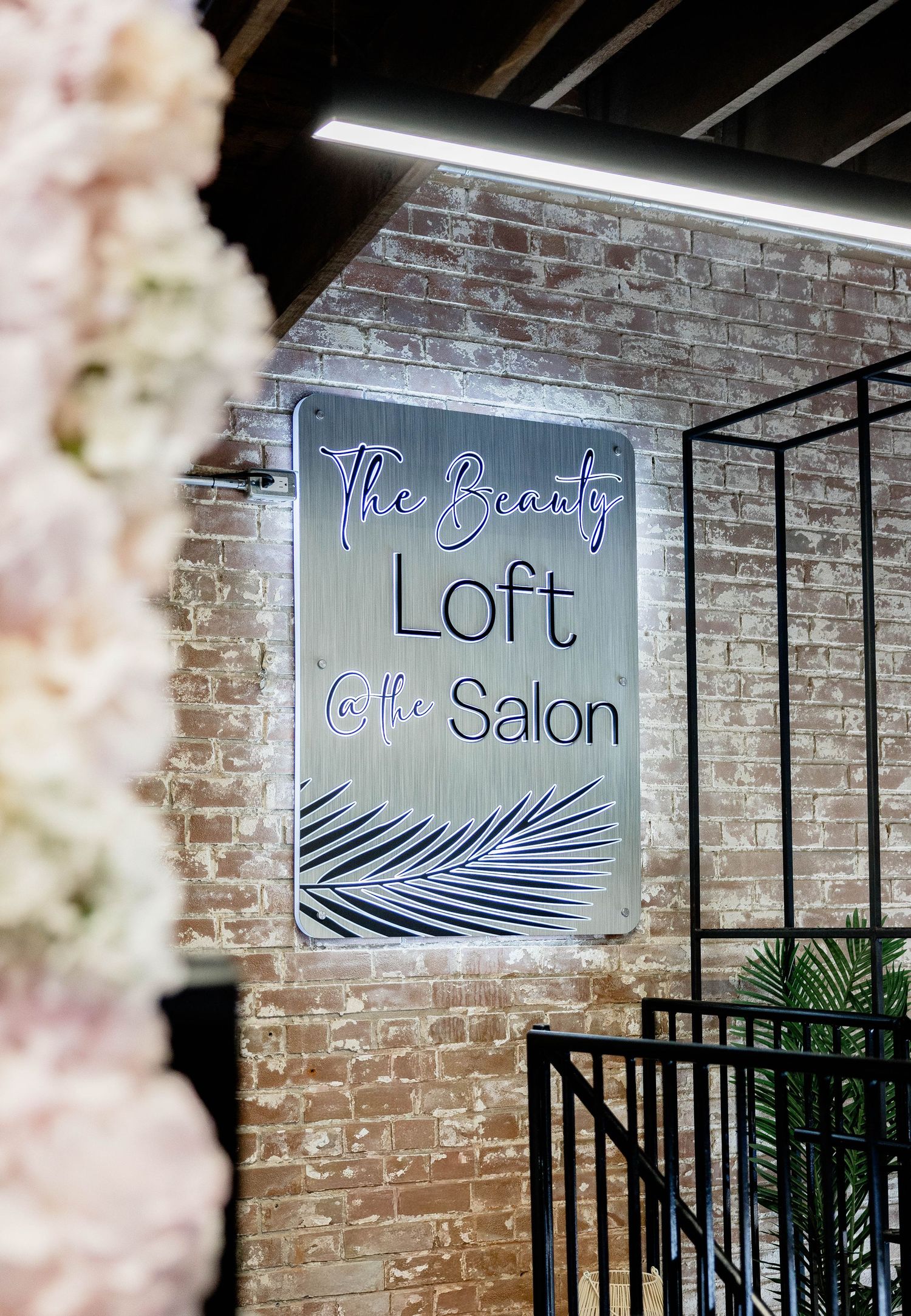 The Beauty Loft at the Salon sign on exposed brick wall with floral decor.