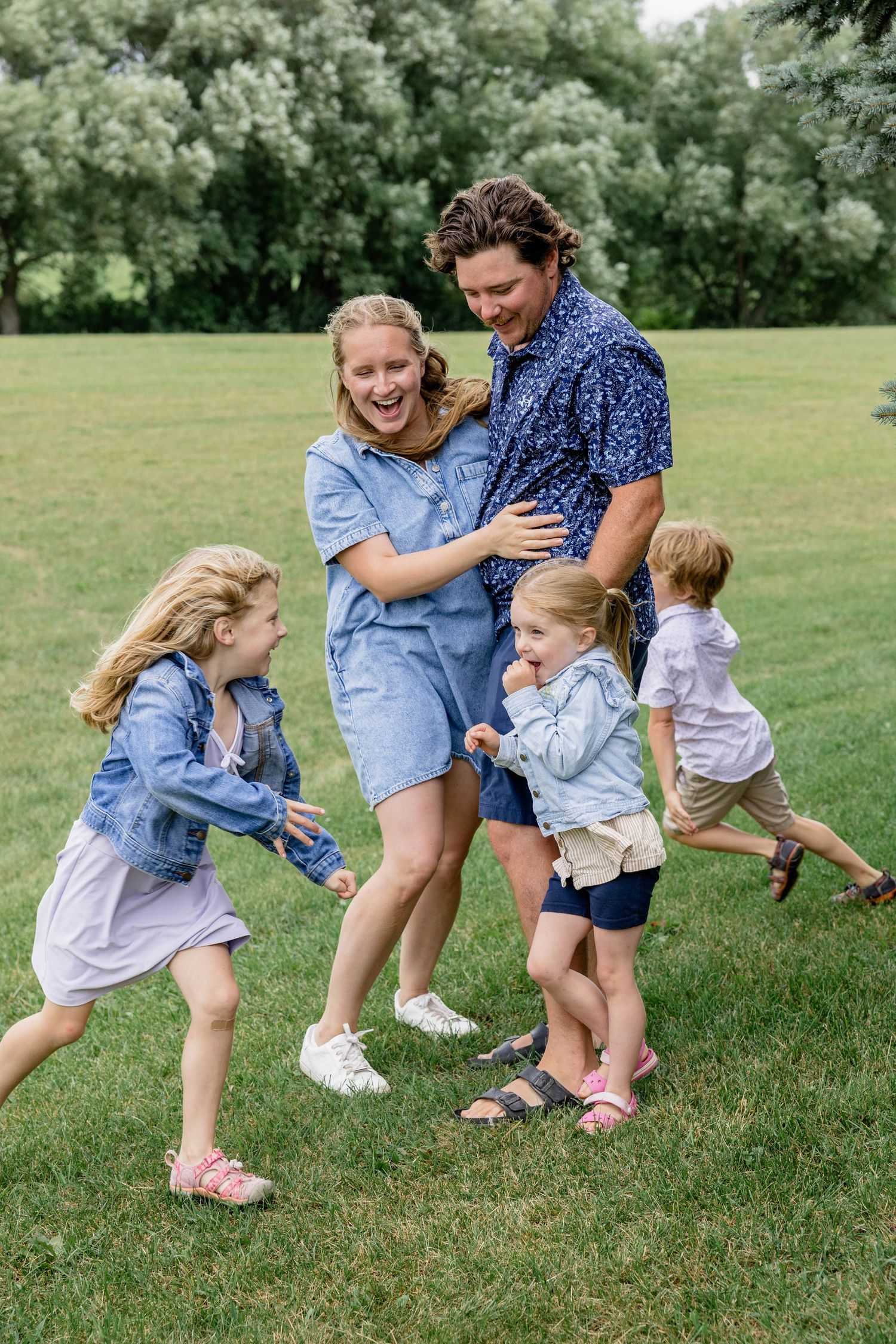 Happy family with three young children playing and laughing together on a green lawn in a park.