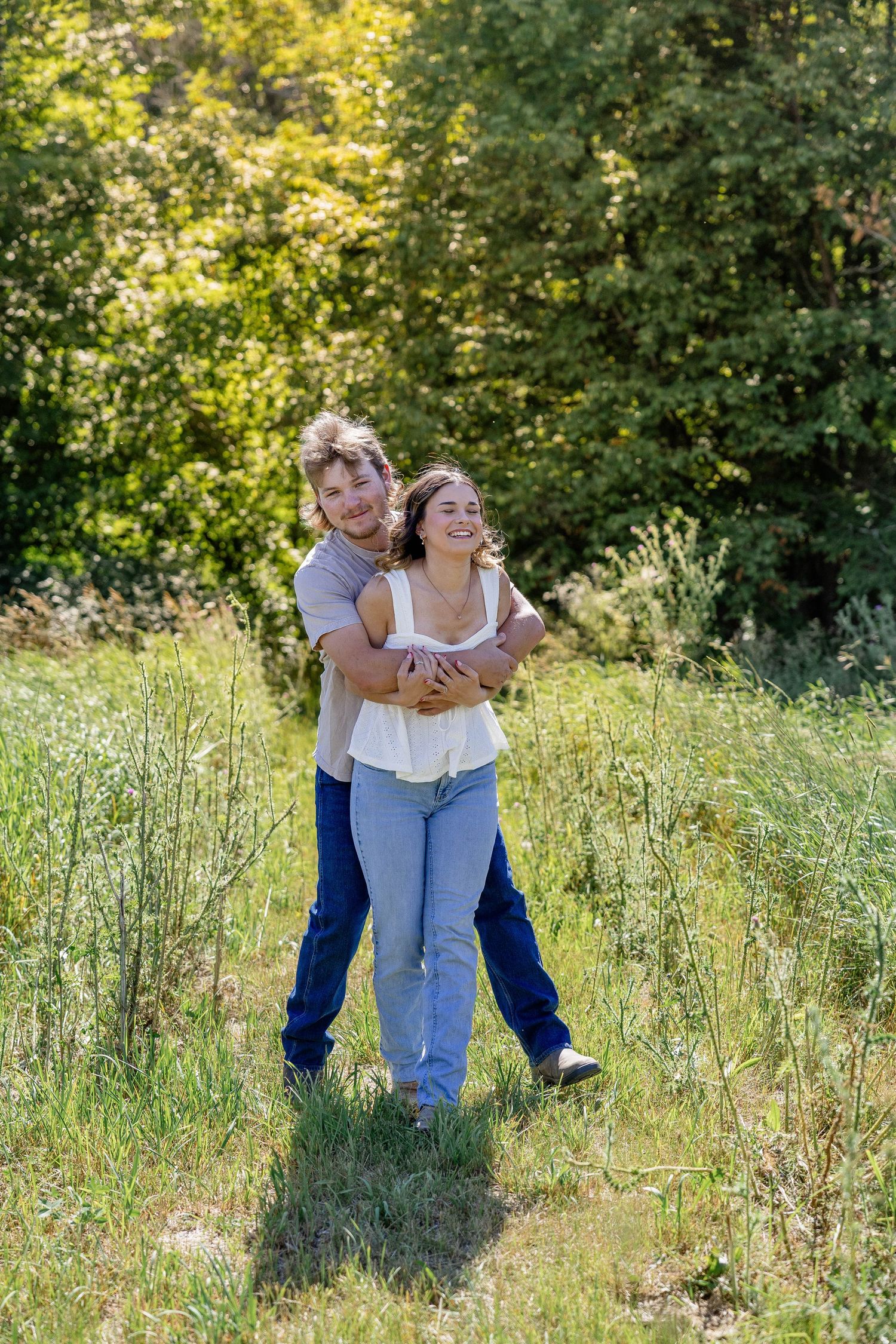 Happy couple embracing outdoors in a green meadow, laughing together on a sunny day.