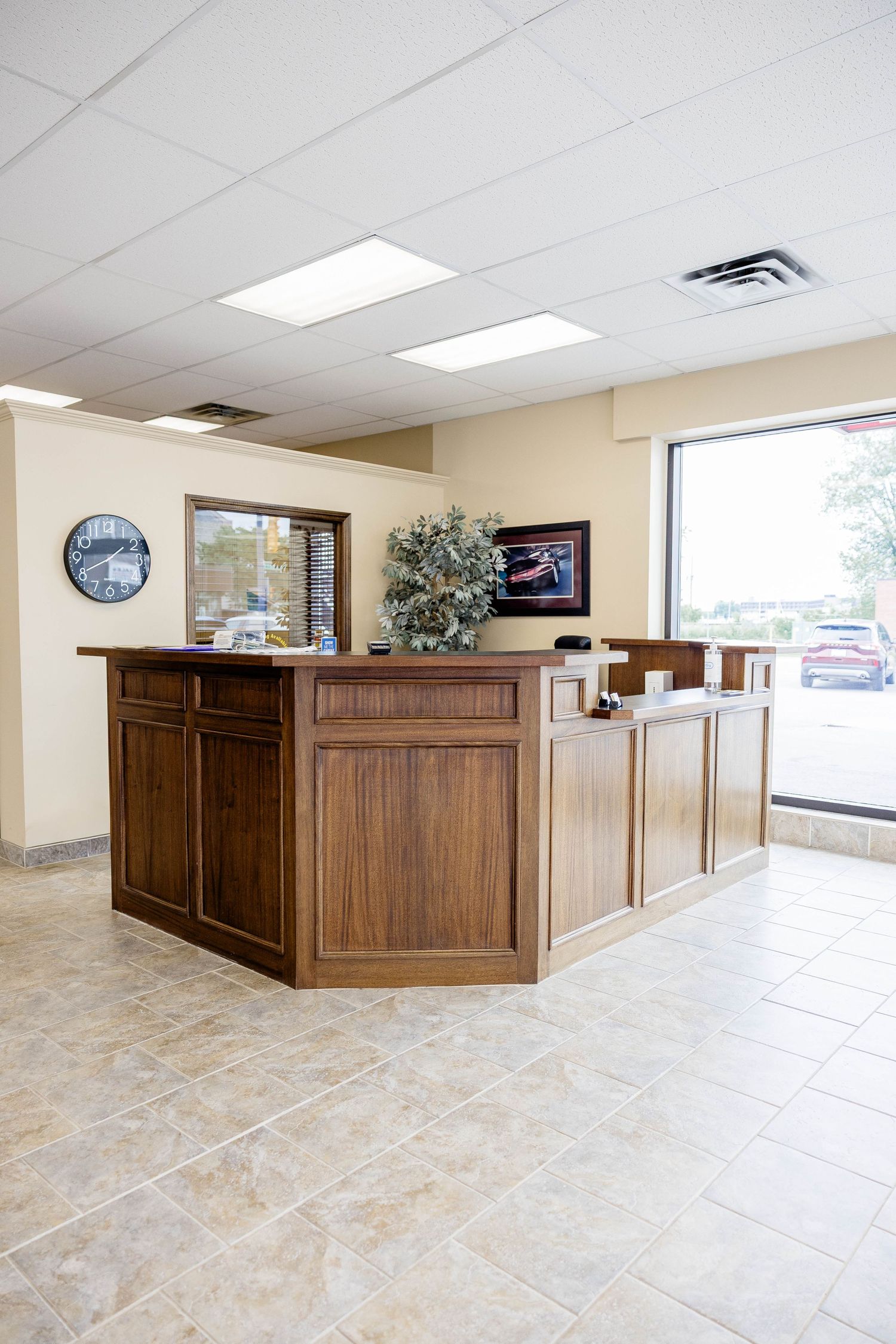 Modern car dealership reception desk in wood finish with decorative plant and large front window.