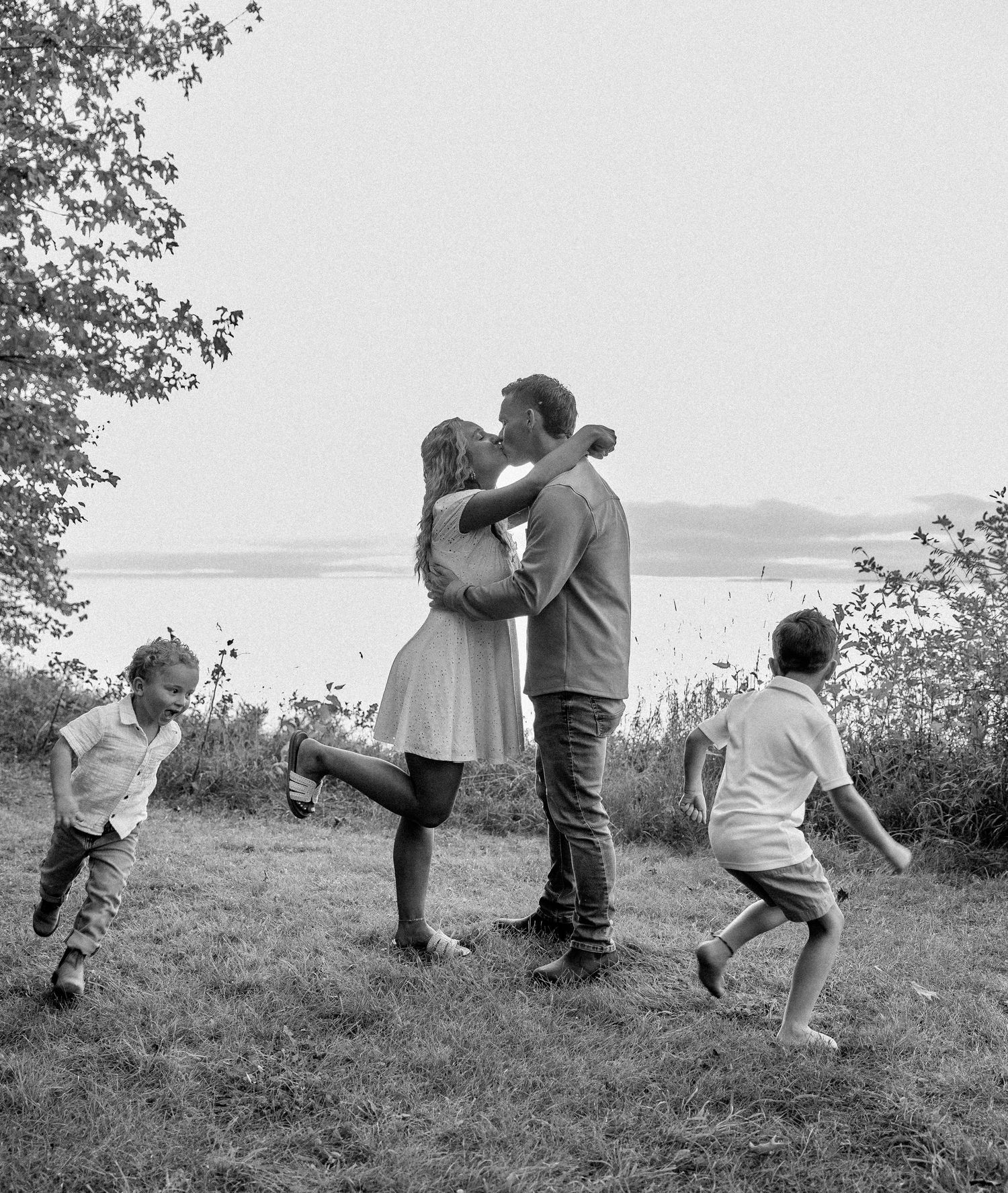 A couple kisses while their children play around them in a scenic outdoor setting.