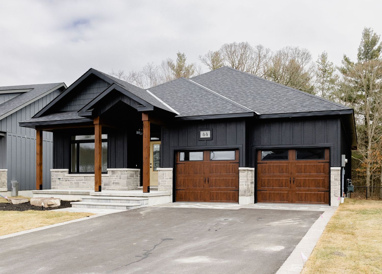 Dark charcoal craftsman bungalow with wood garage doors, stone accents, and covered front porch.