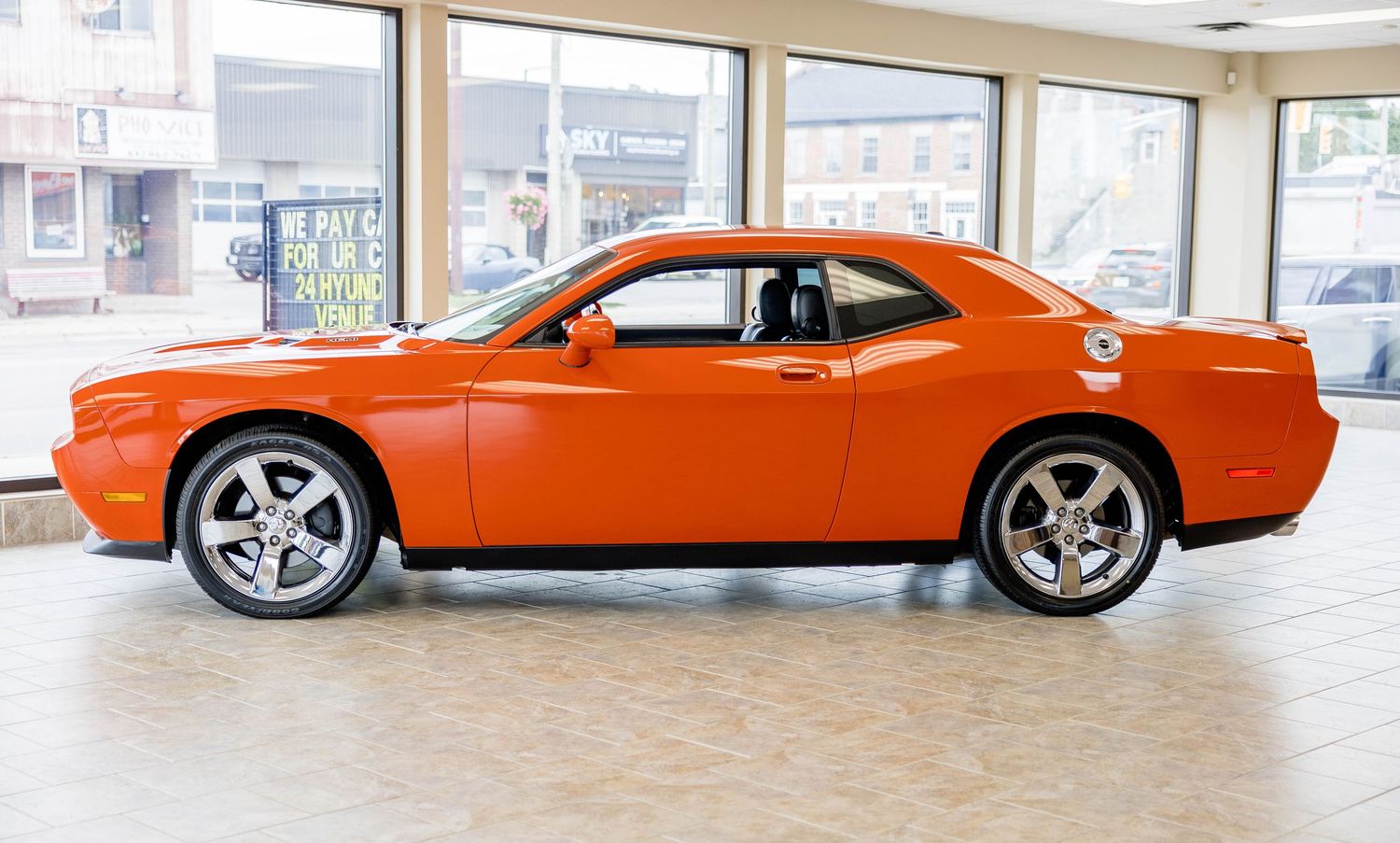 Bright orange Dodge Challenger muscle car displayed inside a car dealership showroom.