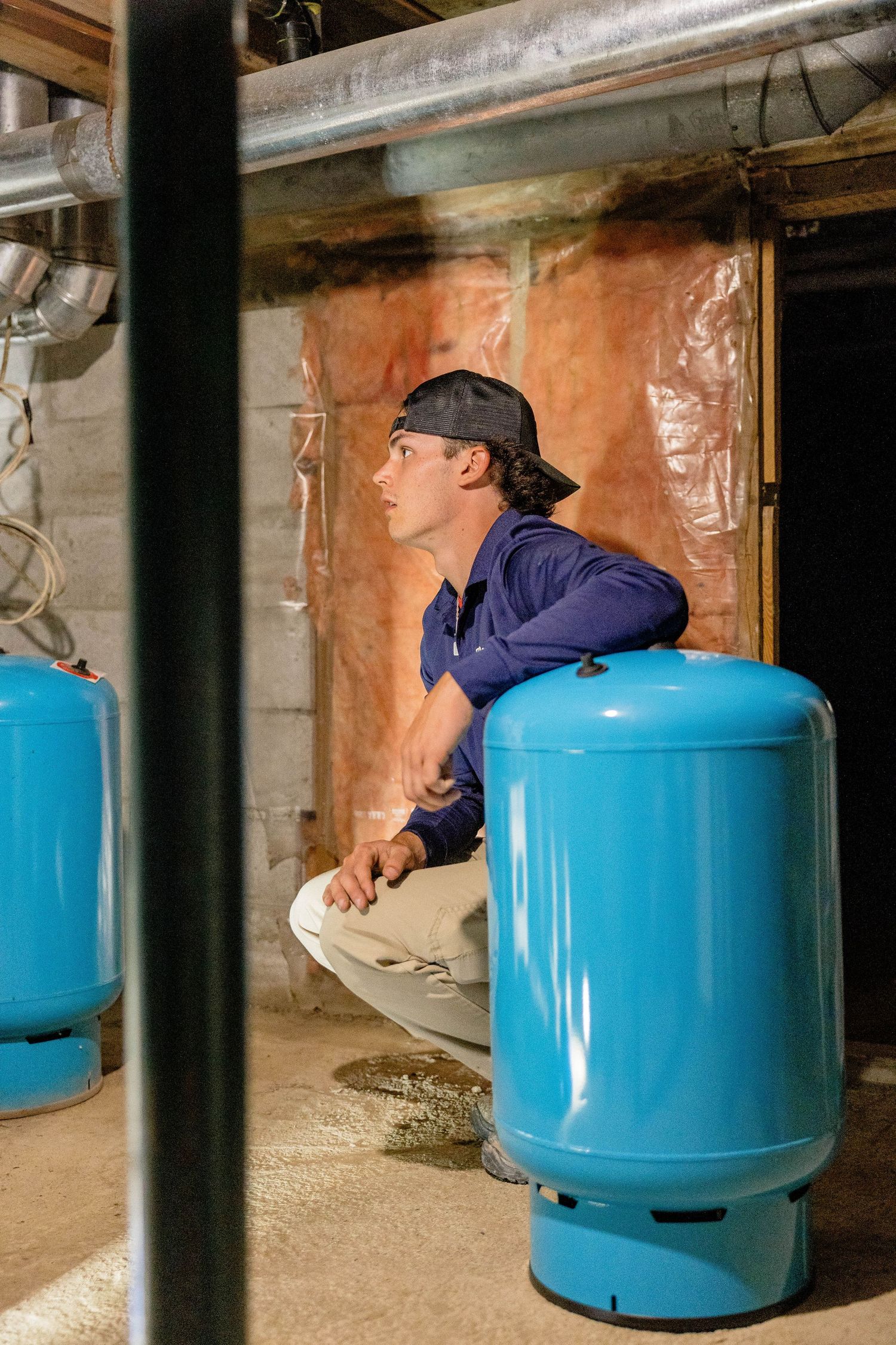 Plumbing technician examining blue pressure tanks in a basement utility room.