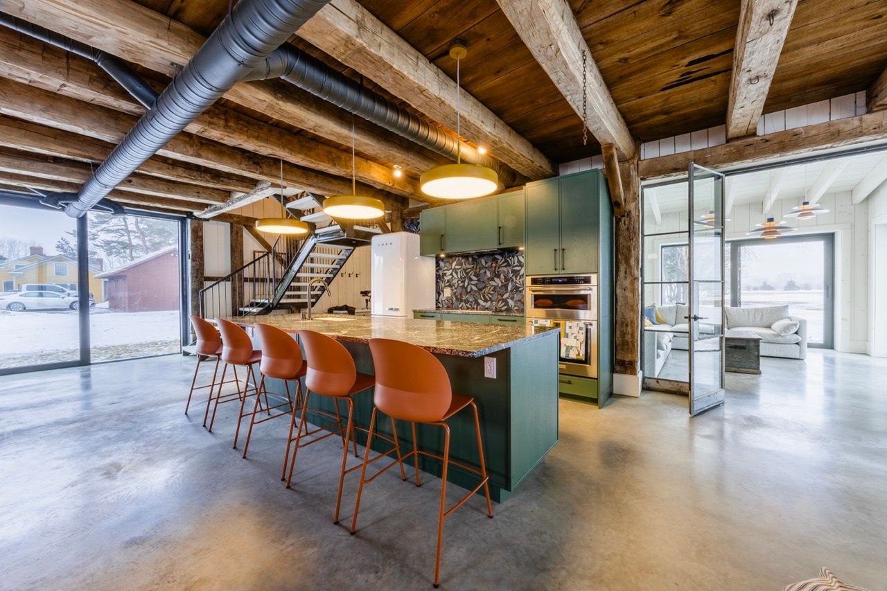 Modern barn conversion kitchen with green cabinets, concrete floors, wood beam ceiling, and island seating.