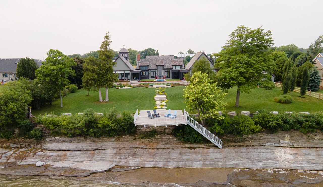 Waterfront estate with a private dock, green lawn, and spacious home surrounded by mature trees.