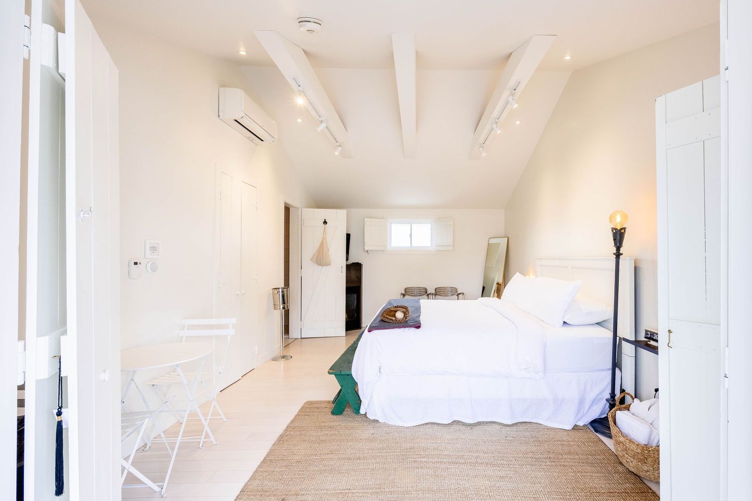 Airy white bedroom with vaulted ceiling, exposed beams, and natural light from window.