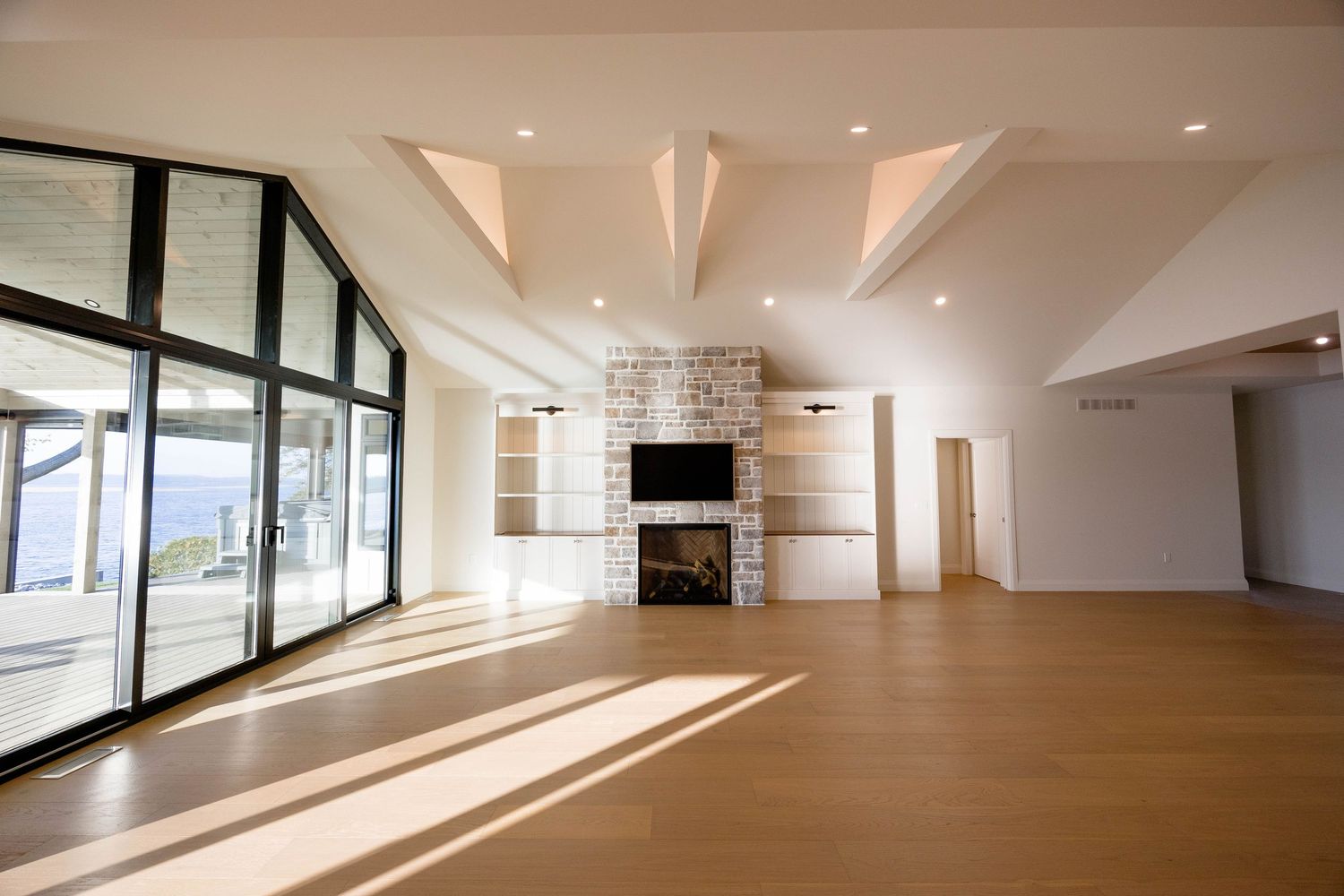 Open-concept living room featuring vaulted ceilings, built-in shelving, stone fireplace, and floor-to-ceiling windows.