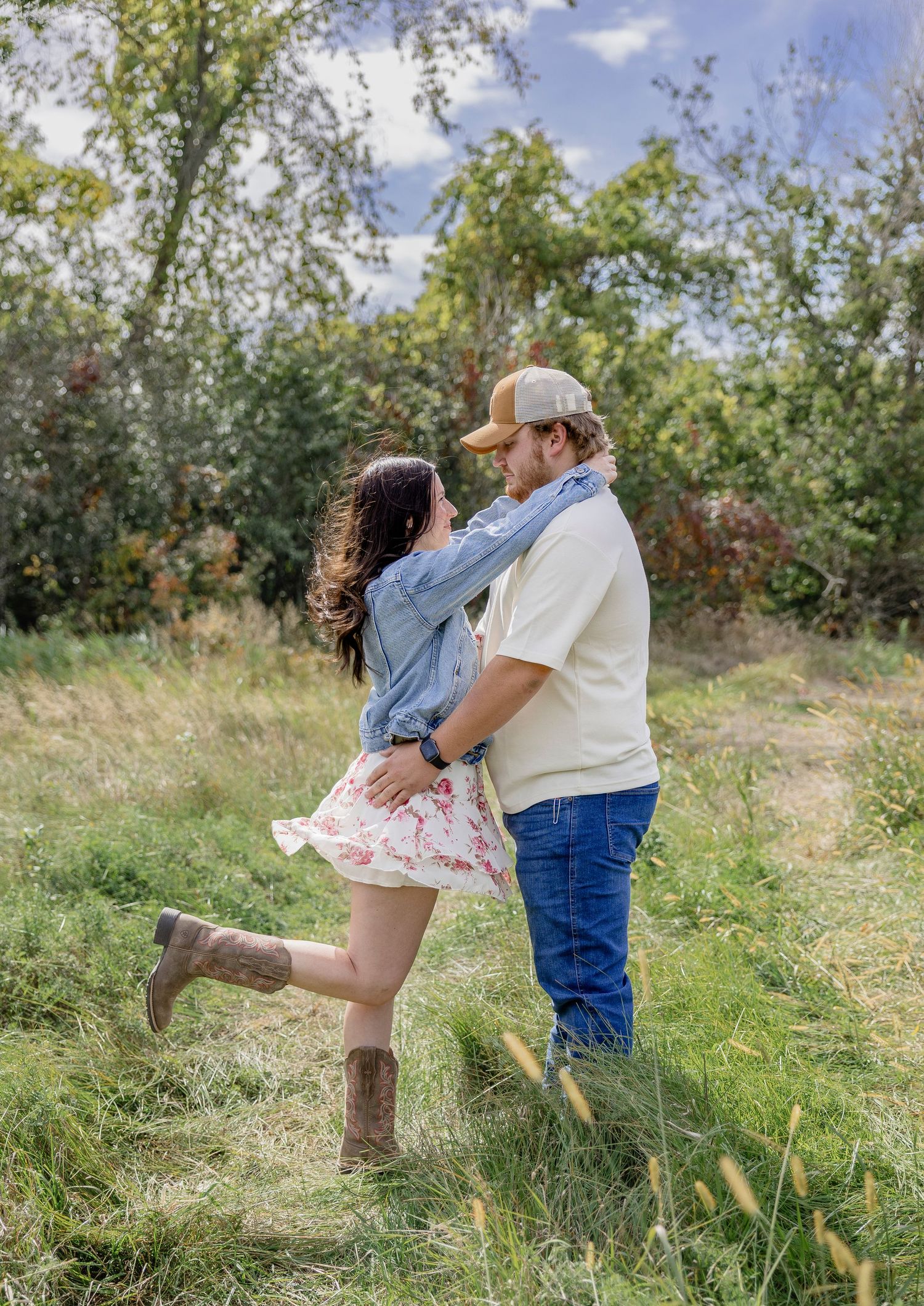 A couple embraces and spins together in a lush green meadow surrounded by autumn trees.