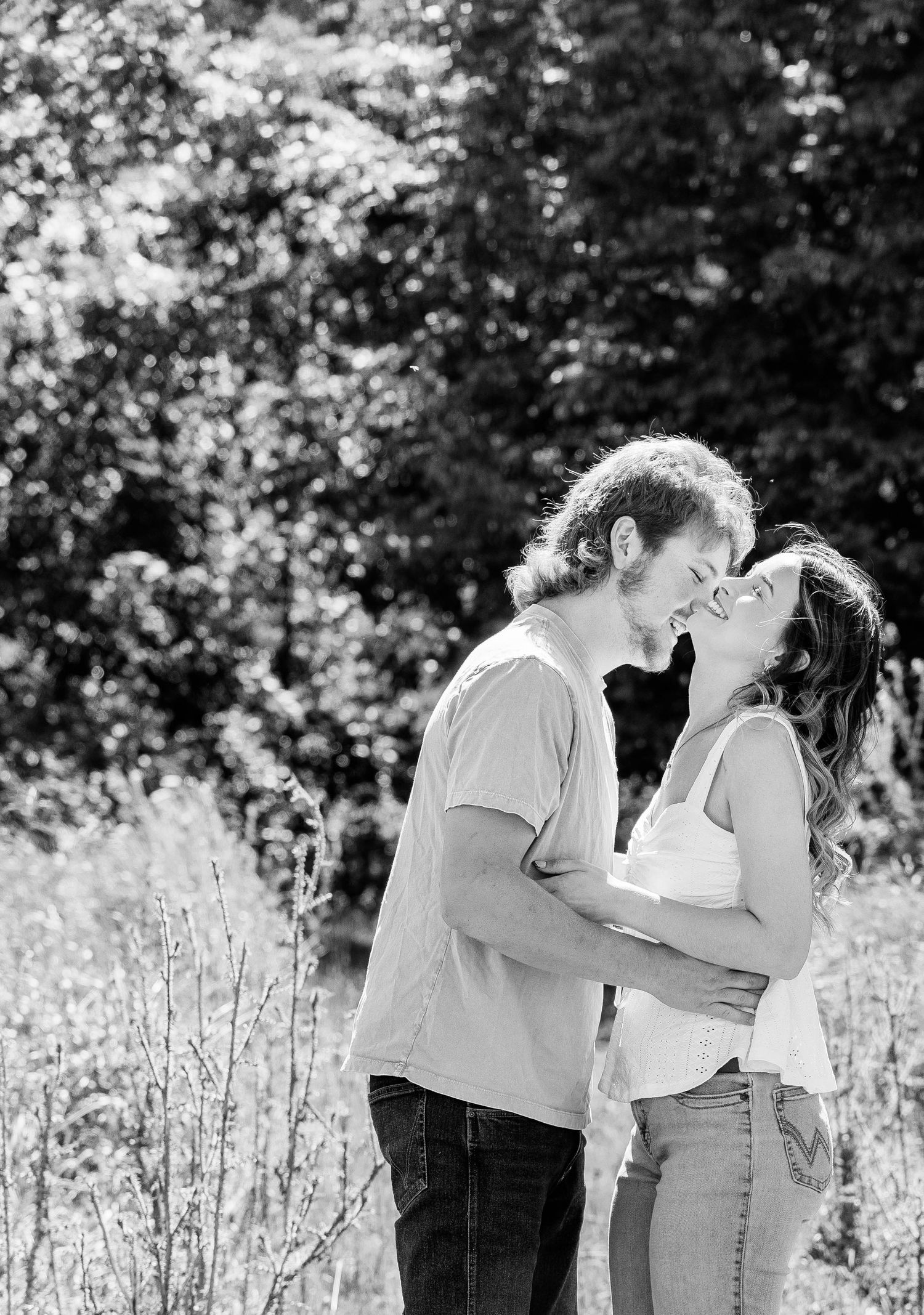 Black and white photo of a romantic couple about to kiss outdoors in a lush garden setting.