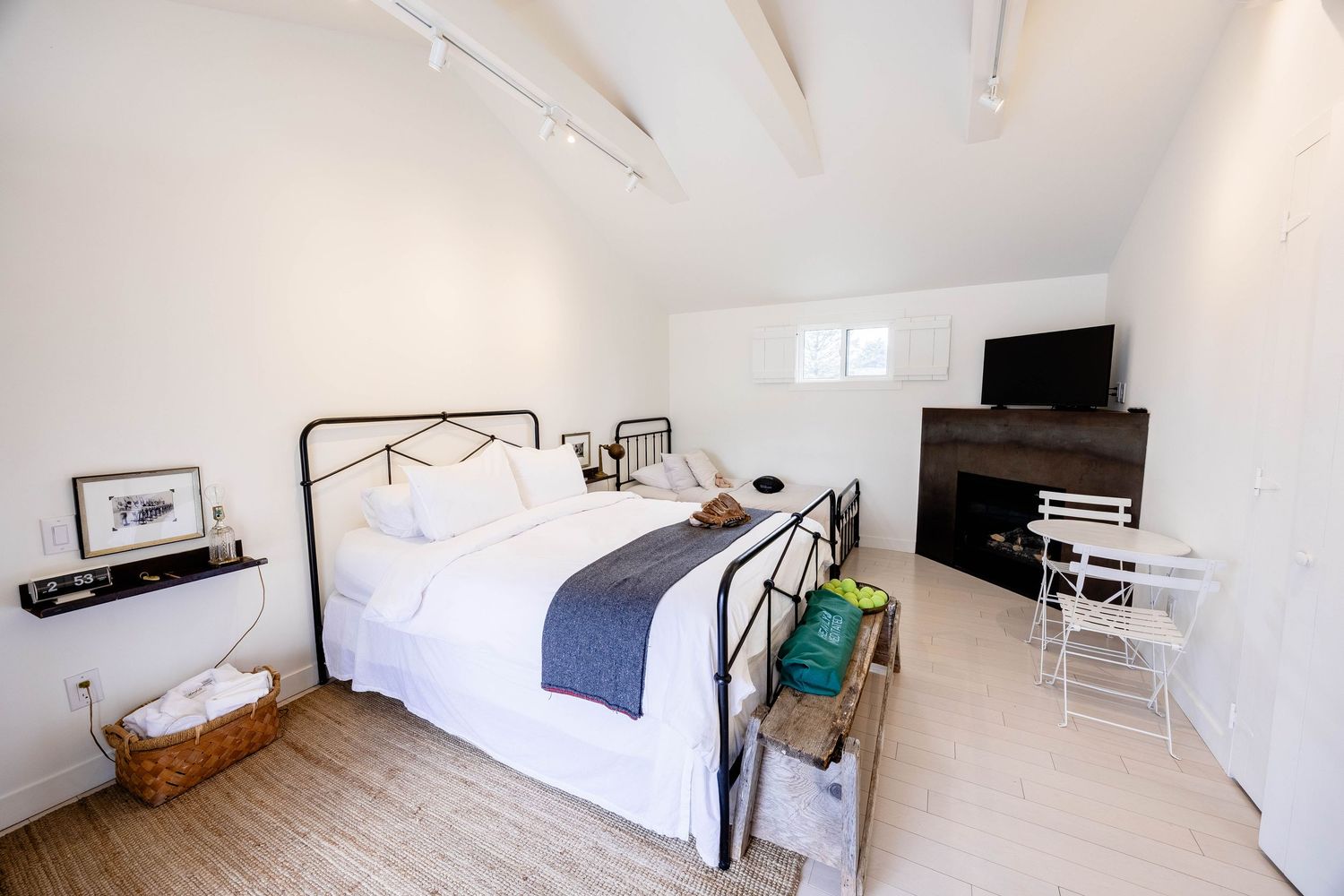 Cozy bedroom with black iron bed frame, fireplace, exposed beam ceiling, and hardwood floors.