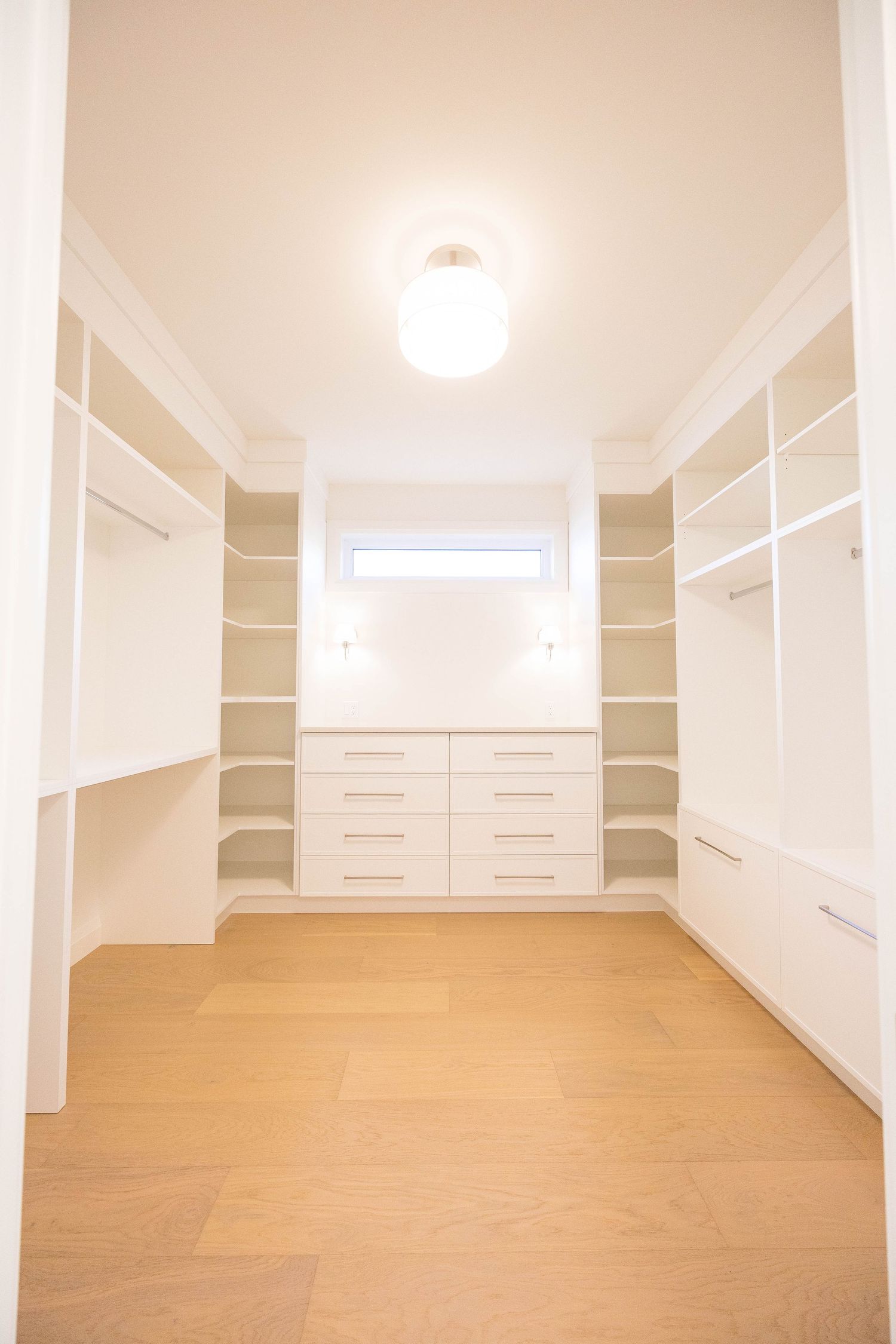 Large walk-in closet with white built-in shelving, drawers, hanging space, and natural wood flooring.