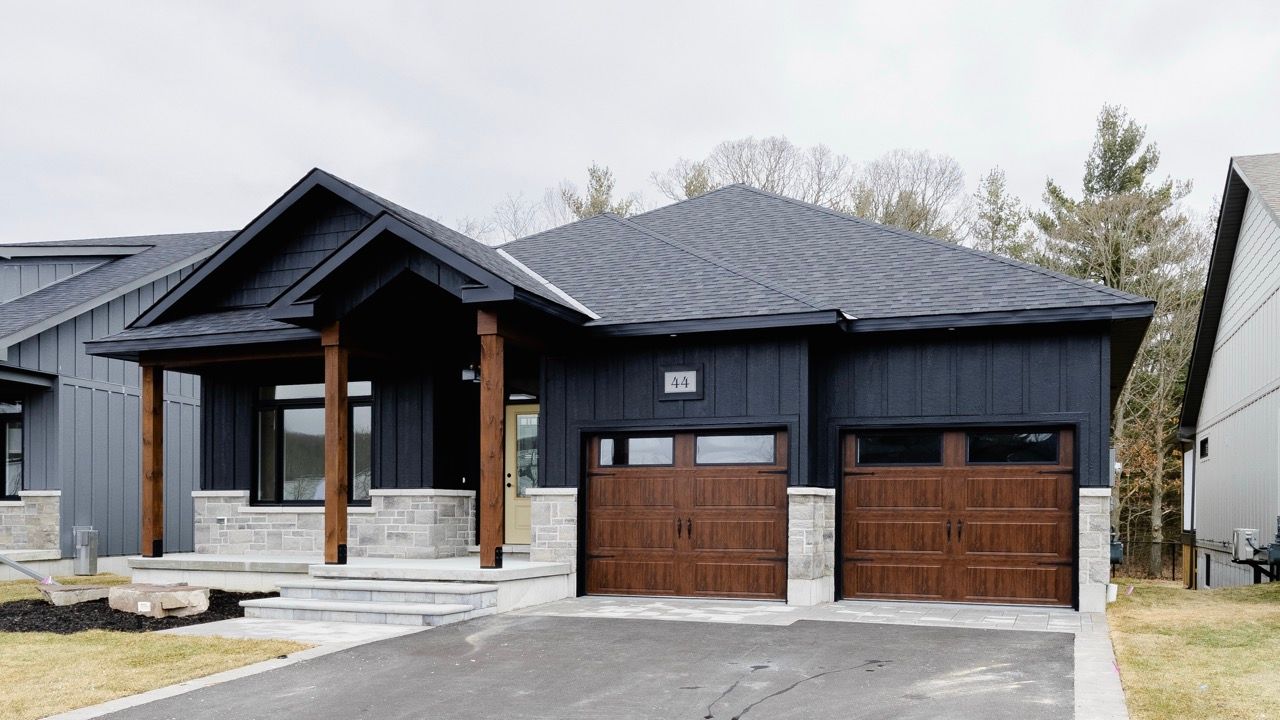 Dark board-and-batten bungalow exterior with stone accents, wood garage doors, and covered porch.