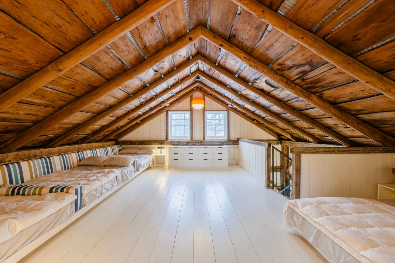 Spacious attic loft with vaulted wood beam ceiling, white plank floors, and multiple beds.