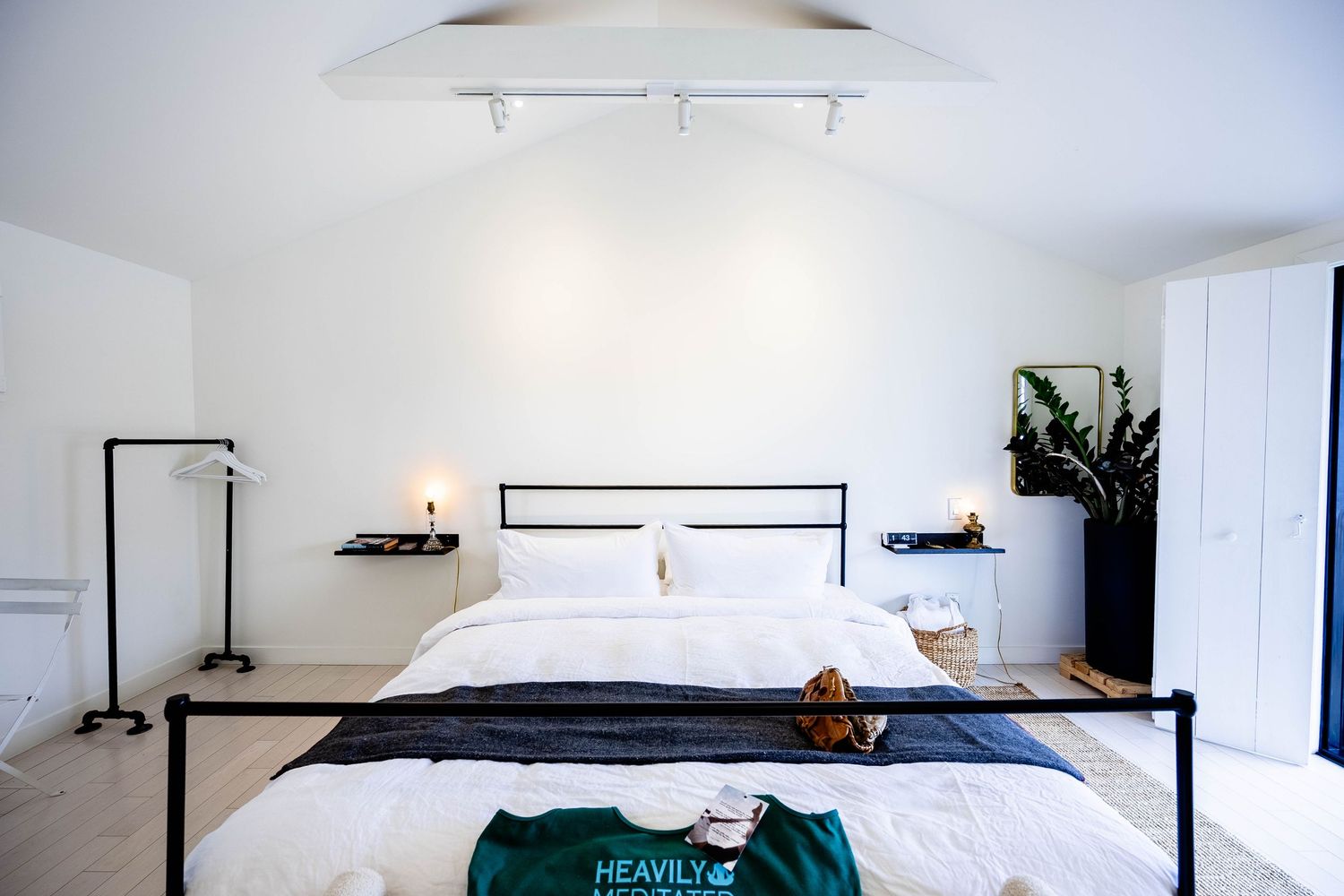 Minimalist white bedroom with black iron bed frame, track lighting, and vaulted ceiling.