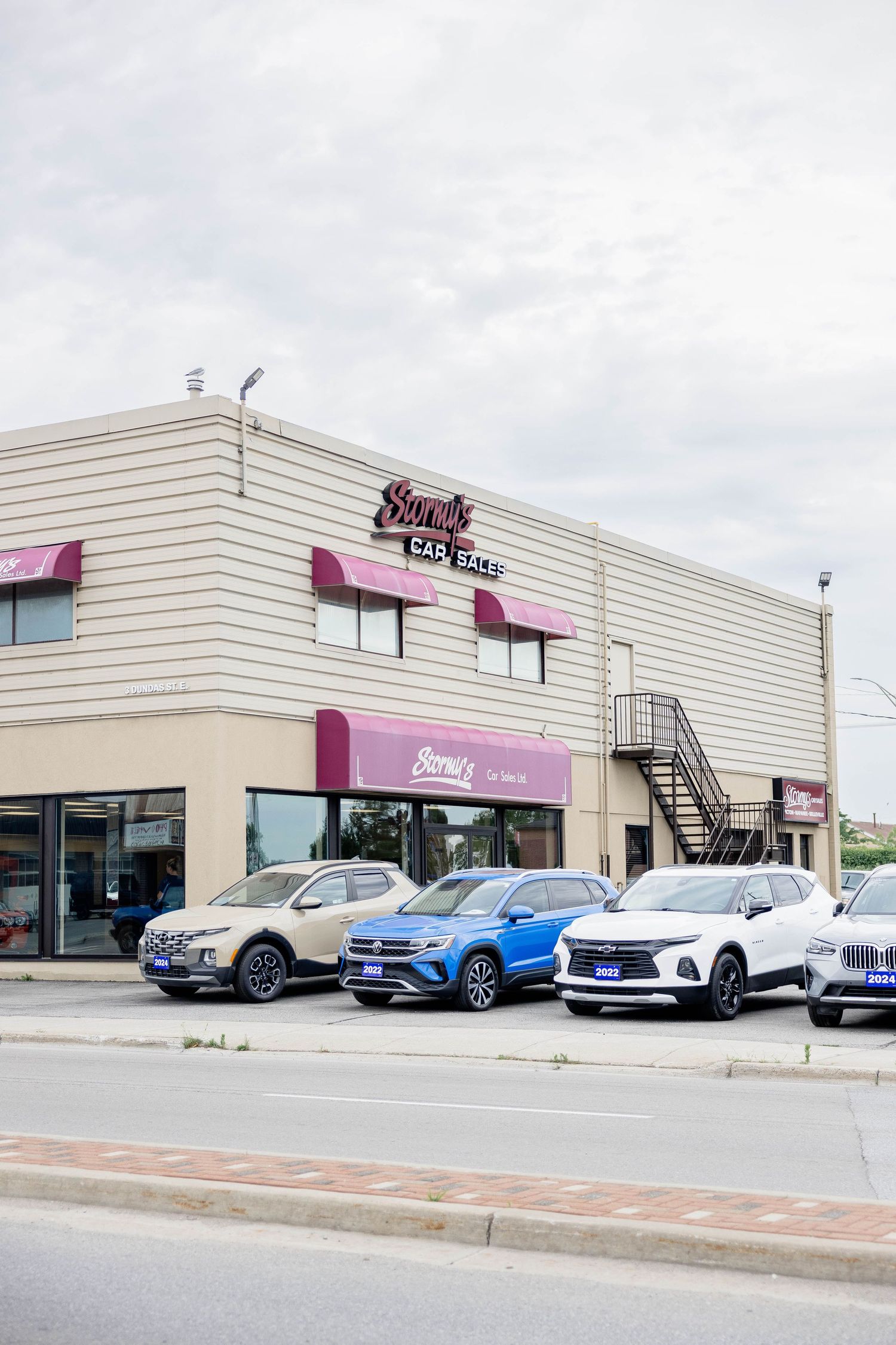 Exterior view of Stormy's Car Sales Ltd. with SUVs parked in front under a cloudy sky.