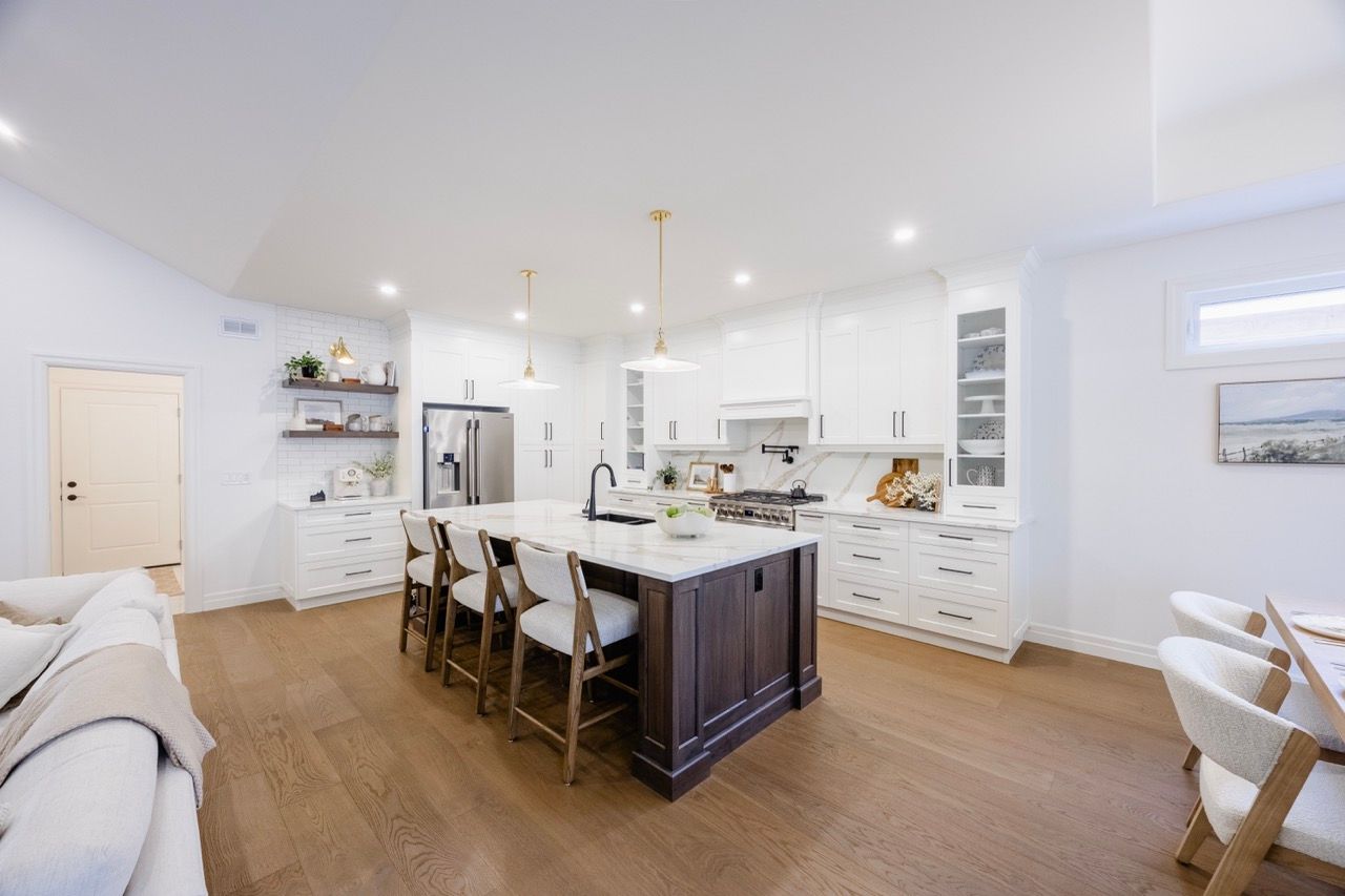 Modern open-concept kitchen with white cabinets, dark island, pendant lights, and hardwood floors in a bright home.