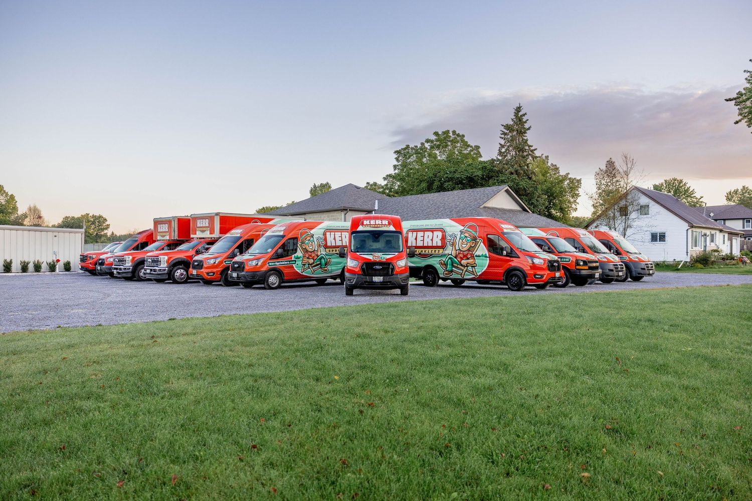 Fleet of red and green branded Kerr service vans parked in a lot at dusk near a residential building.