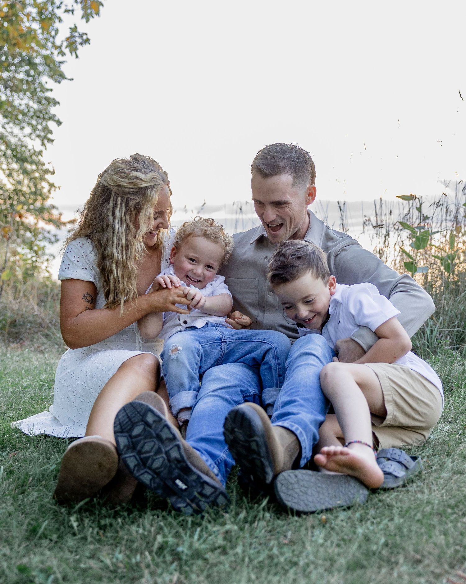 Happy family of four sitting on grass, laughing together outdoors on a sunny day.
