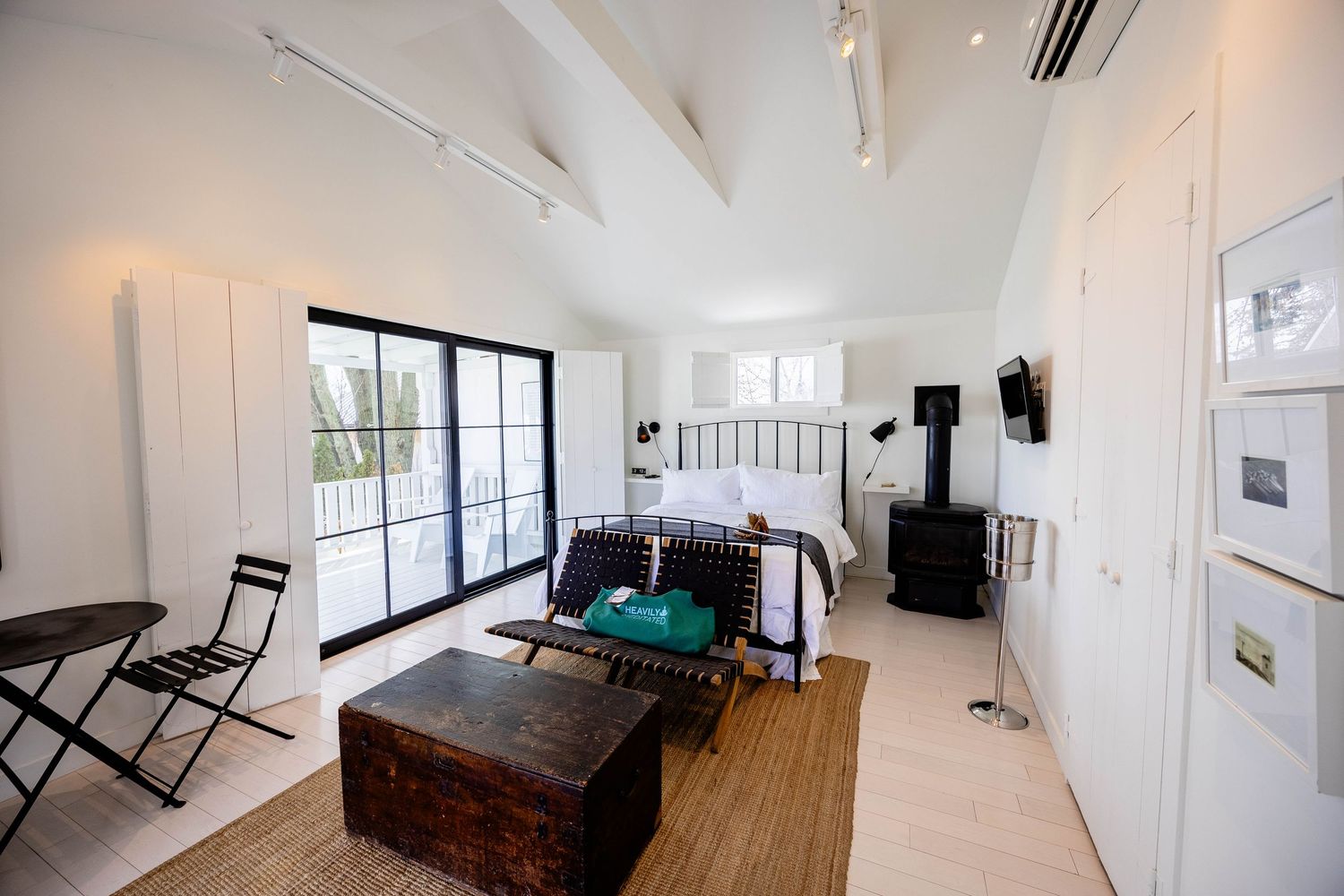 Bright studio bedroom with vaulted ceiling, black iron bed, sliding glass doors, and wood trunk.