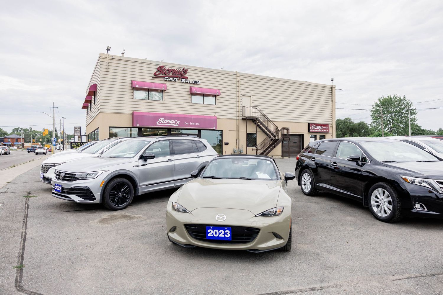 Stormy's Car Sales used car lot featuring 2023 Mazda MX-5 and VW Tiguan on display outside.